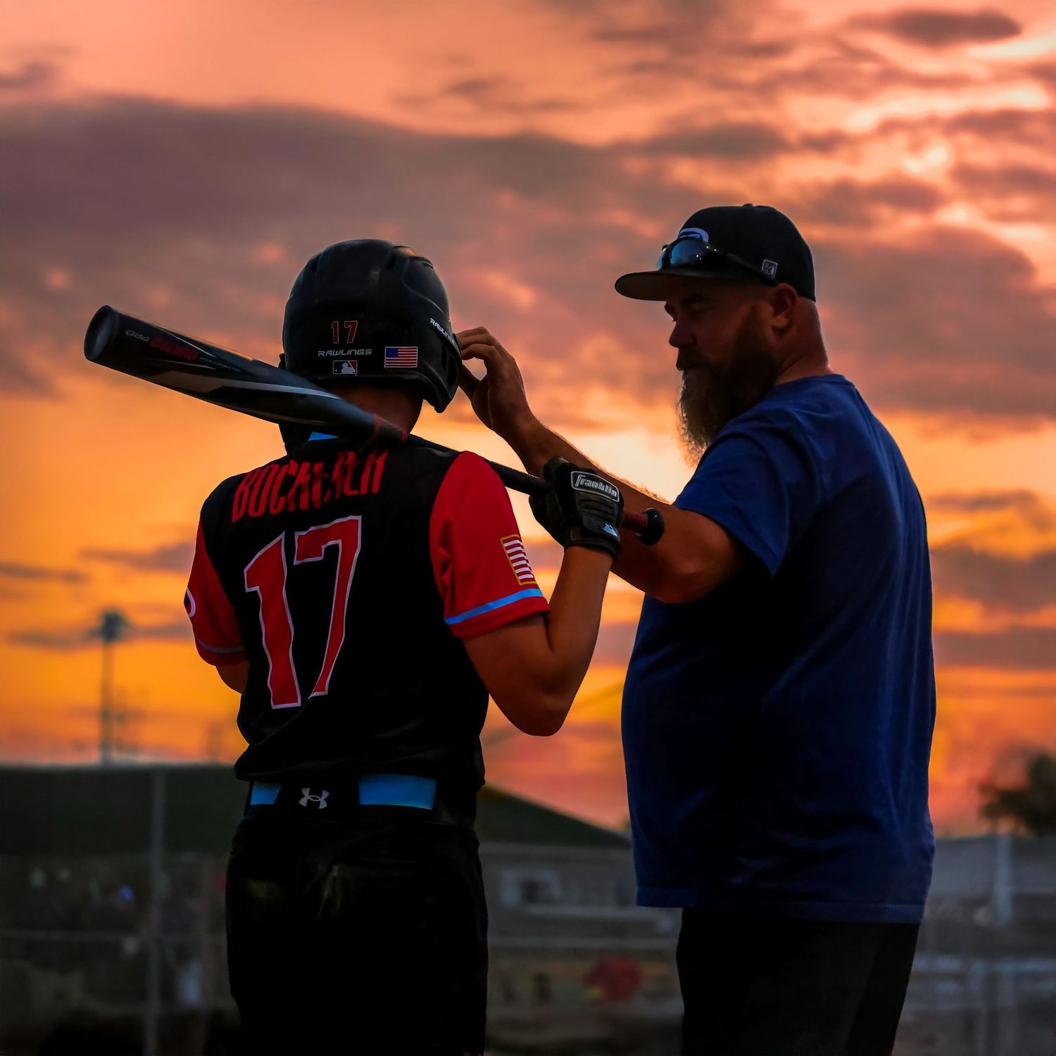 Baseball coach instructs player with bat during sunset game.