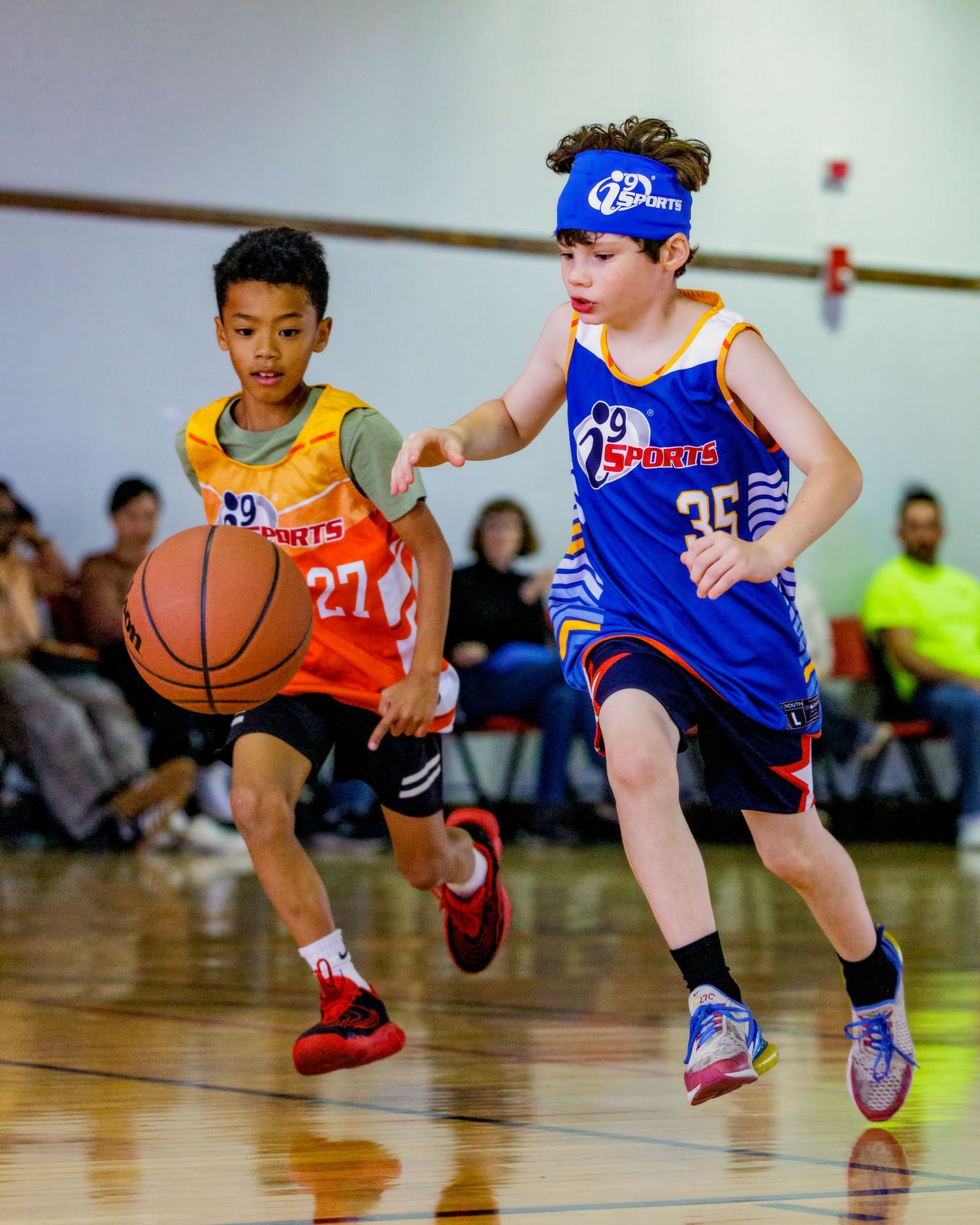 Young basketball players in orange and blue uniforms dribbling and playing on a wooden court.
