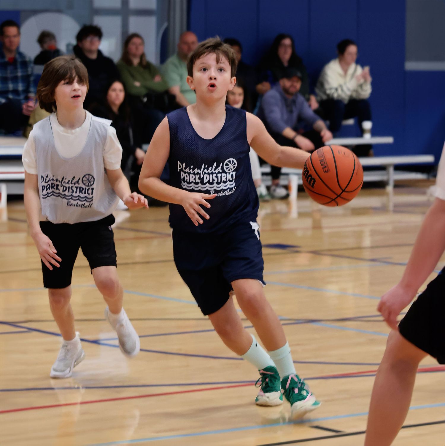Young basketball players in action during a youth league game in a gymnasium with blue walls.