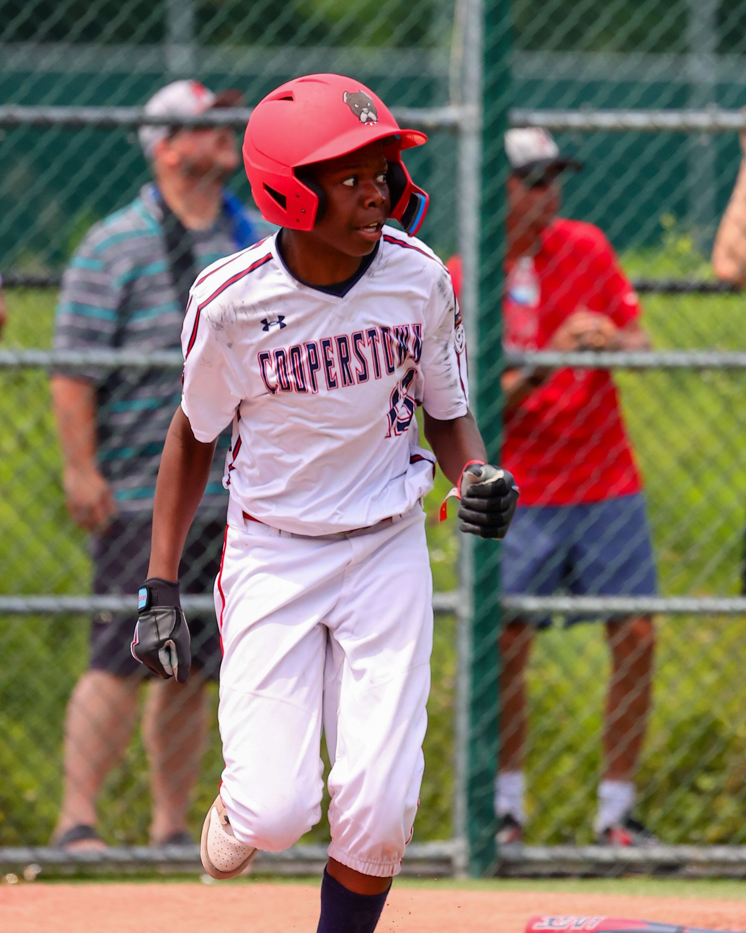 Baseball player in white uniform and red helmet takes a powerful swing during a game at an outdoor field.