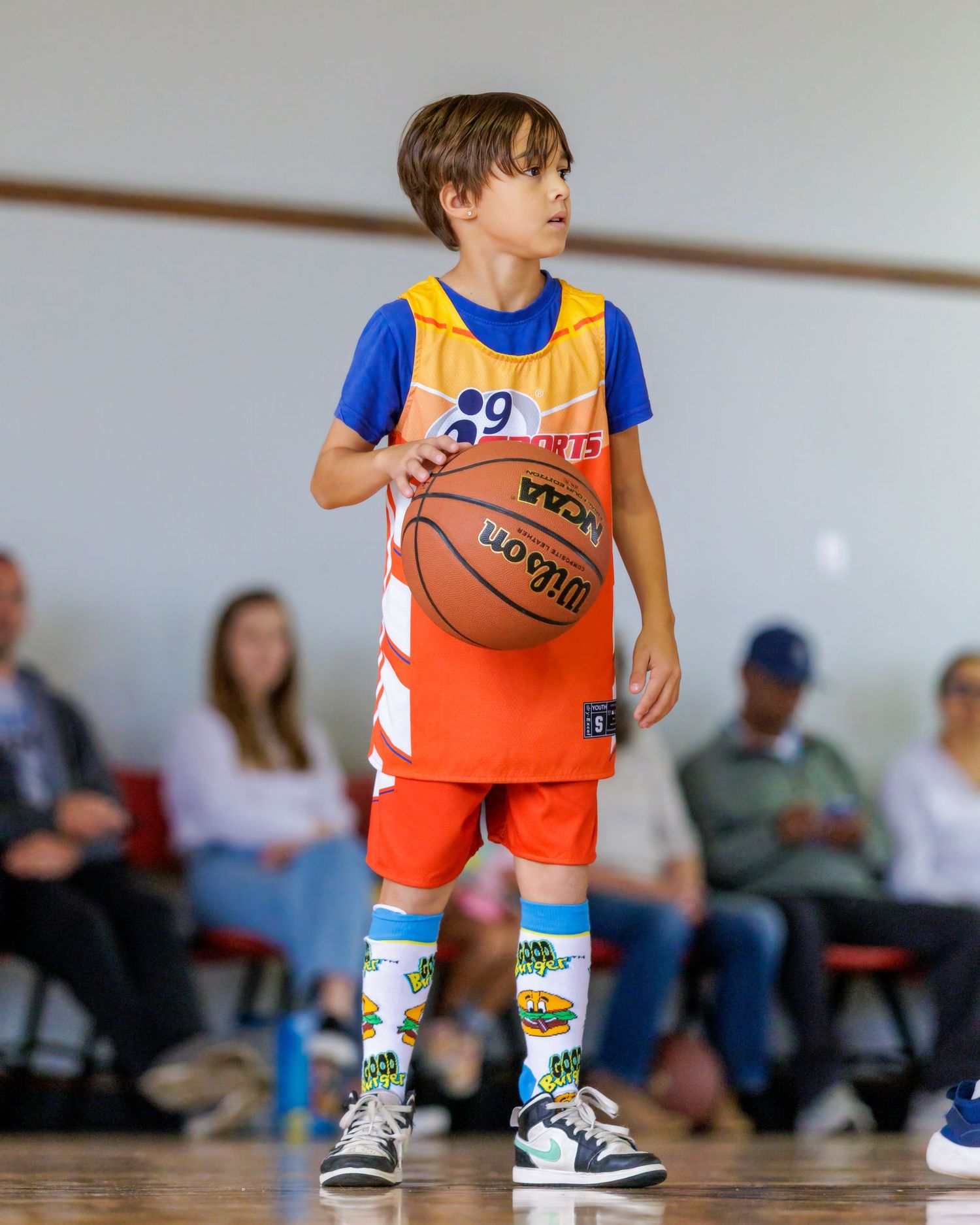 Young basketball player in orange jersey and blue shirt dribbles ball during practice session.