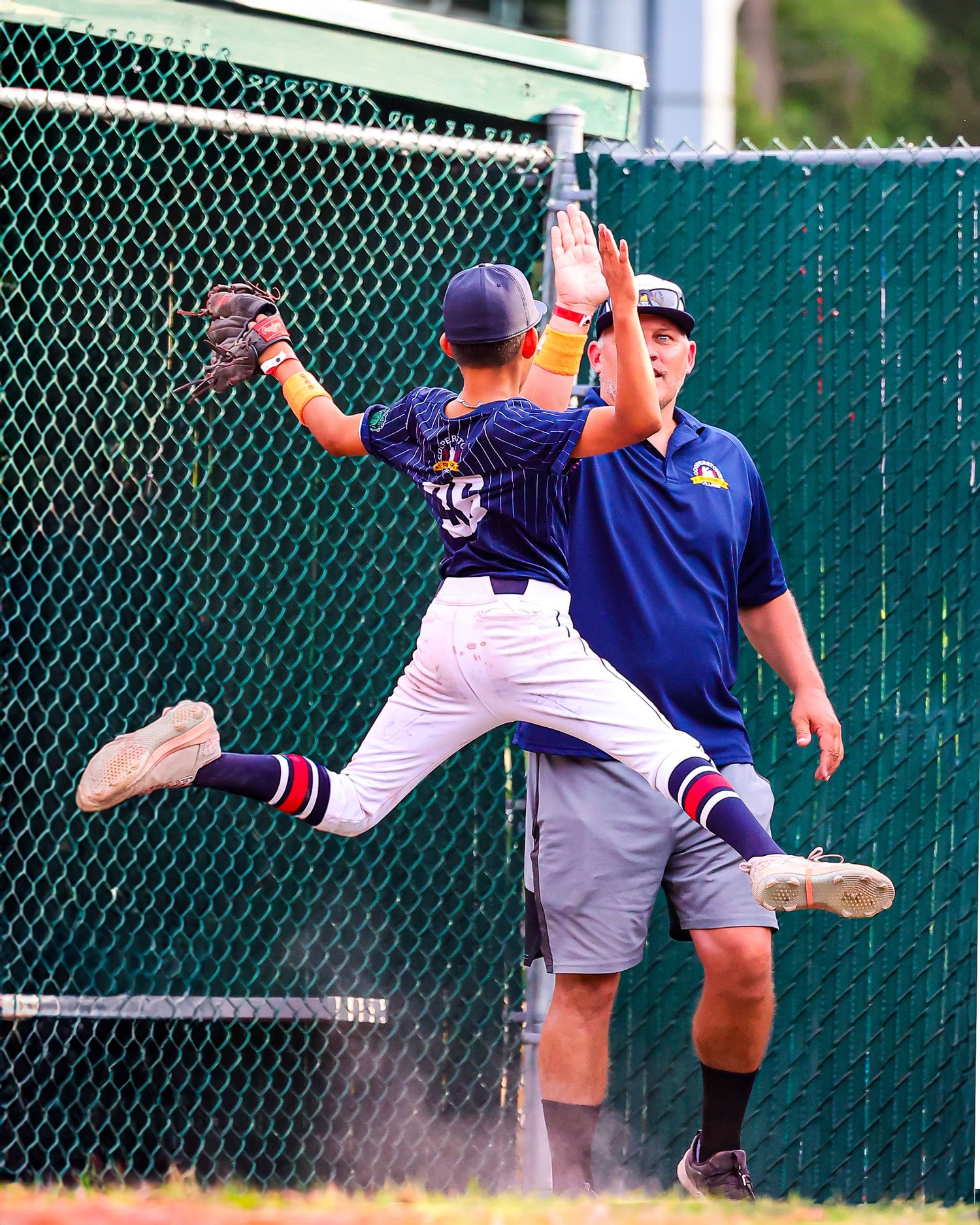 Baseball player in blue uniform makes a dramatic catch against a chain link fence during a game.