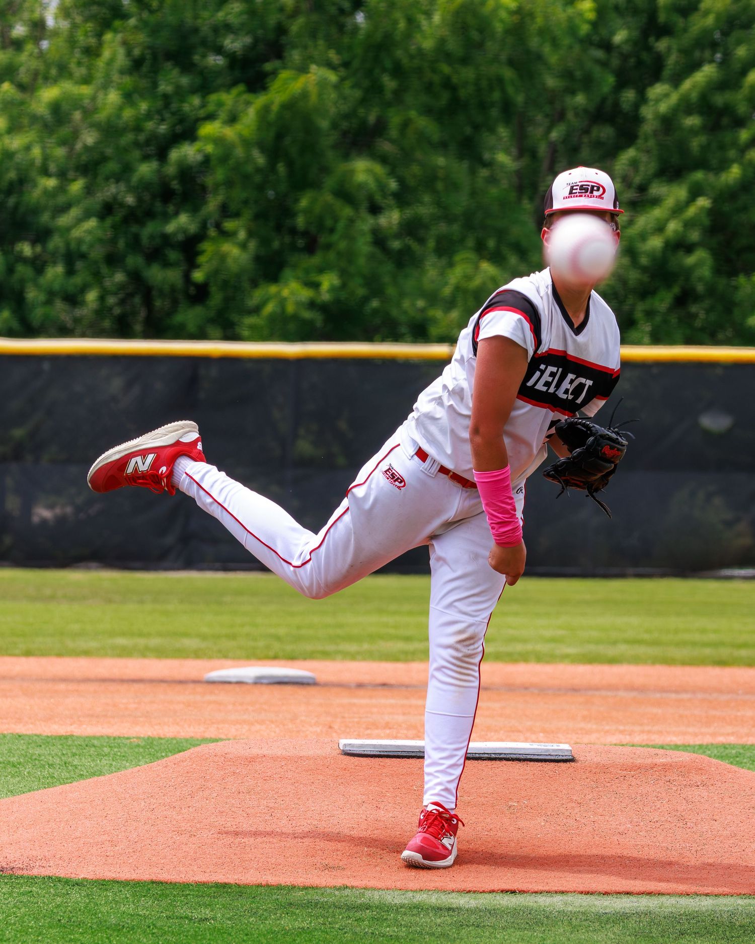 Baseball pitcher in white and pink uniform mid-throw on mound during outdoor game.