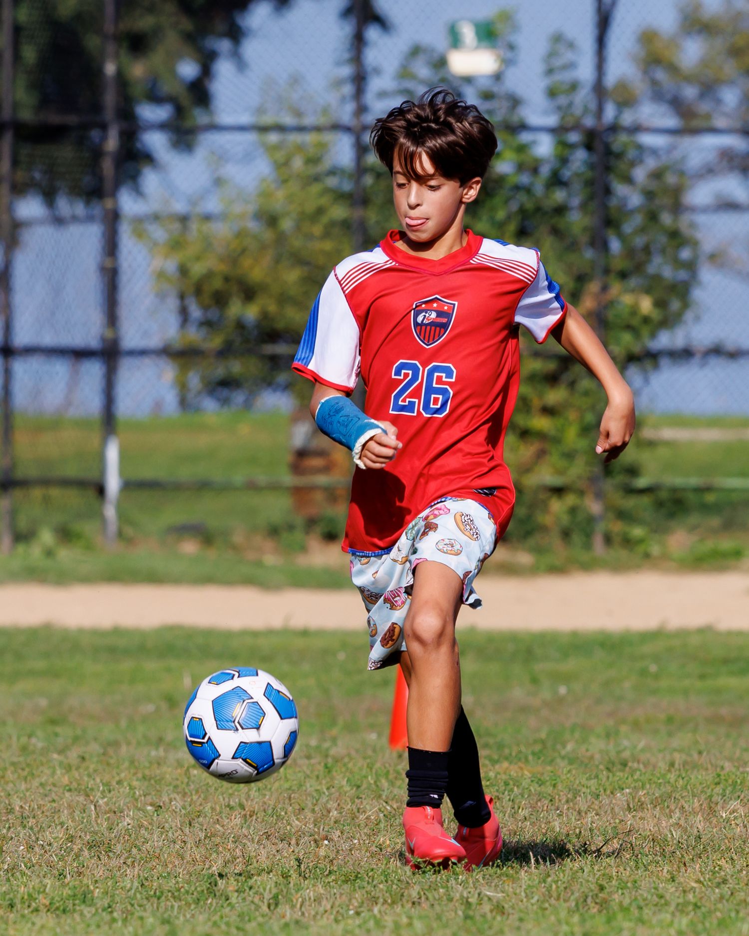 Young boy in red number 26 soccer jersey dribbling a ball during a youth soccer game on a grass field.