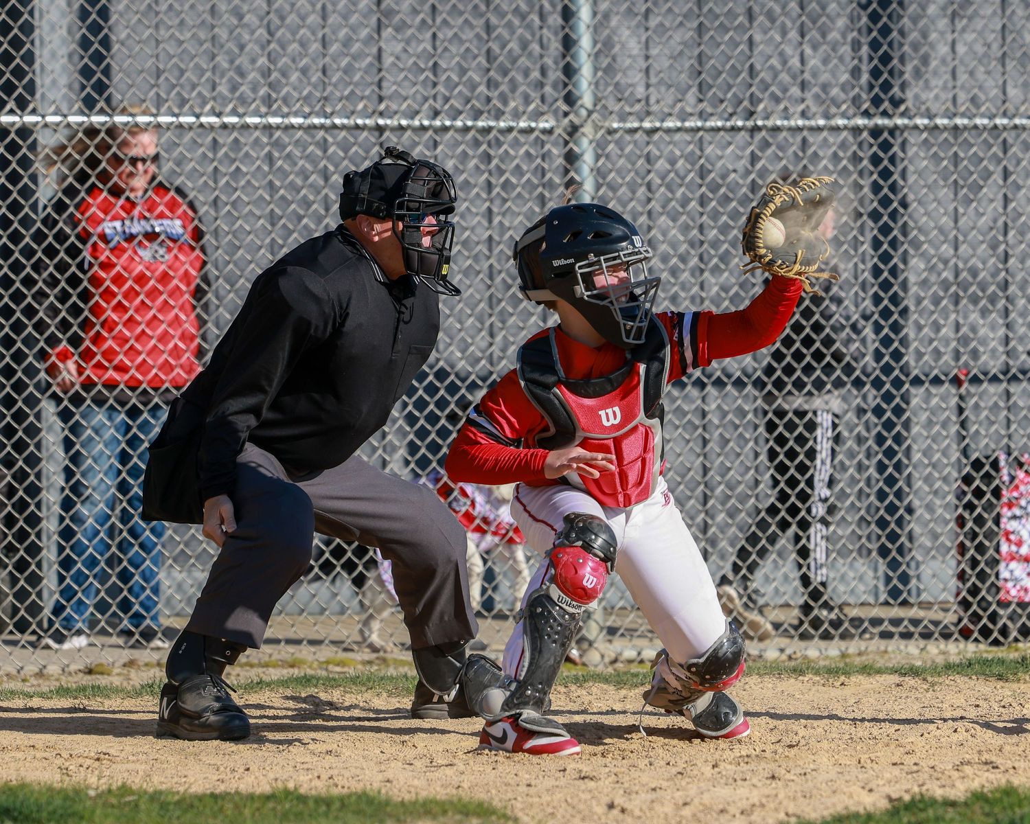 Baseball catcher in red uniform crouching behind home plate during game.