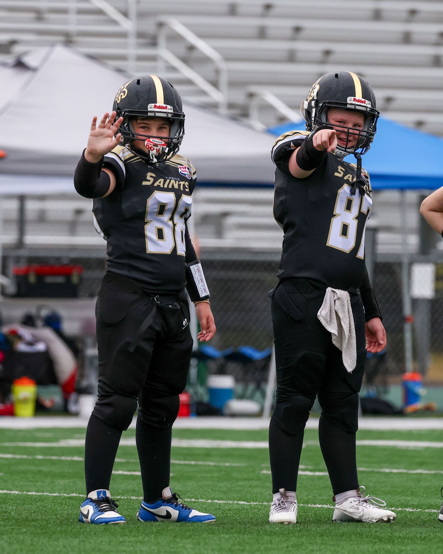 Two youth football players in black Saints uniforms pointing on the field during a game.