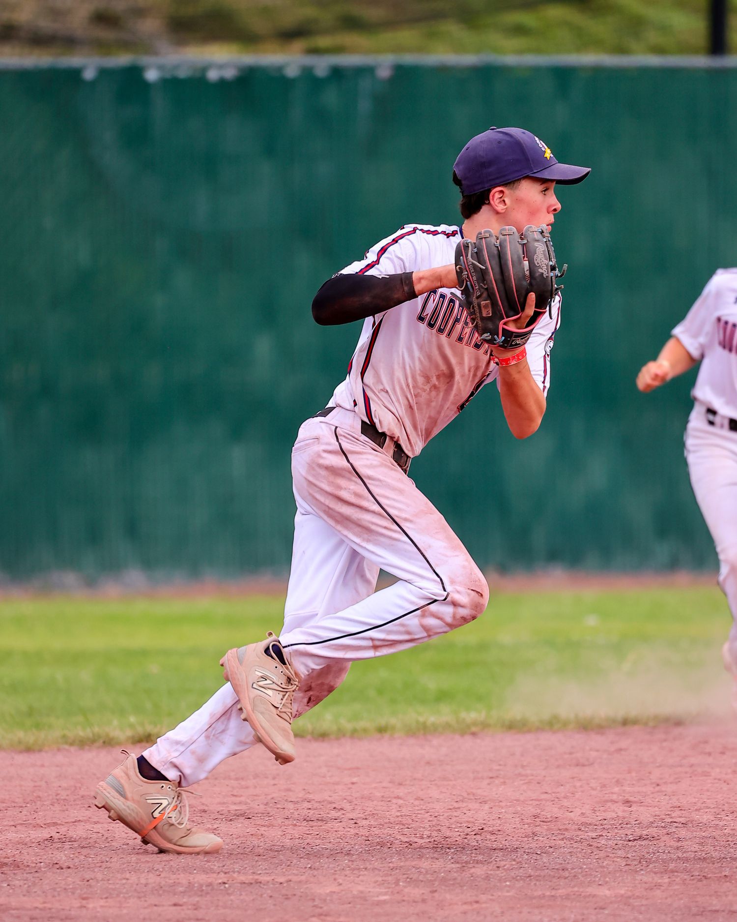 Baseball player crouches down to field a ground ball during infield practice on a sunny day.