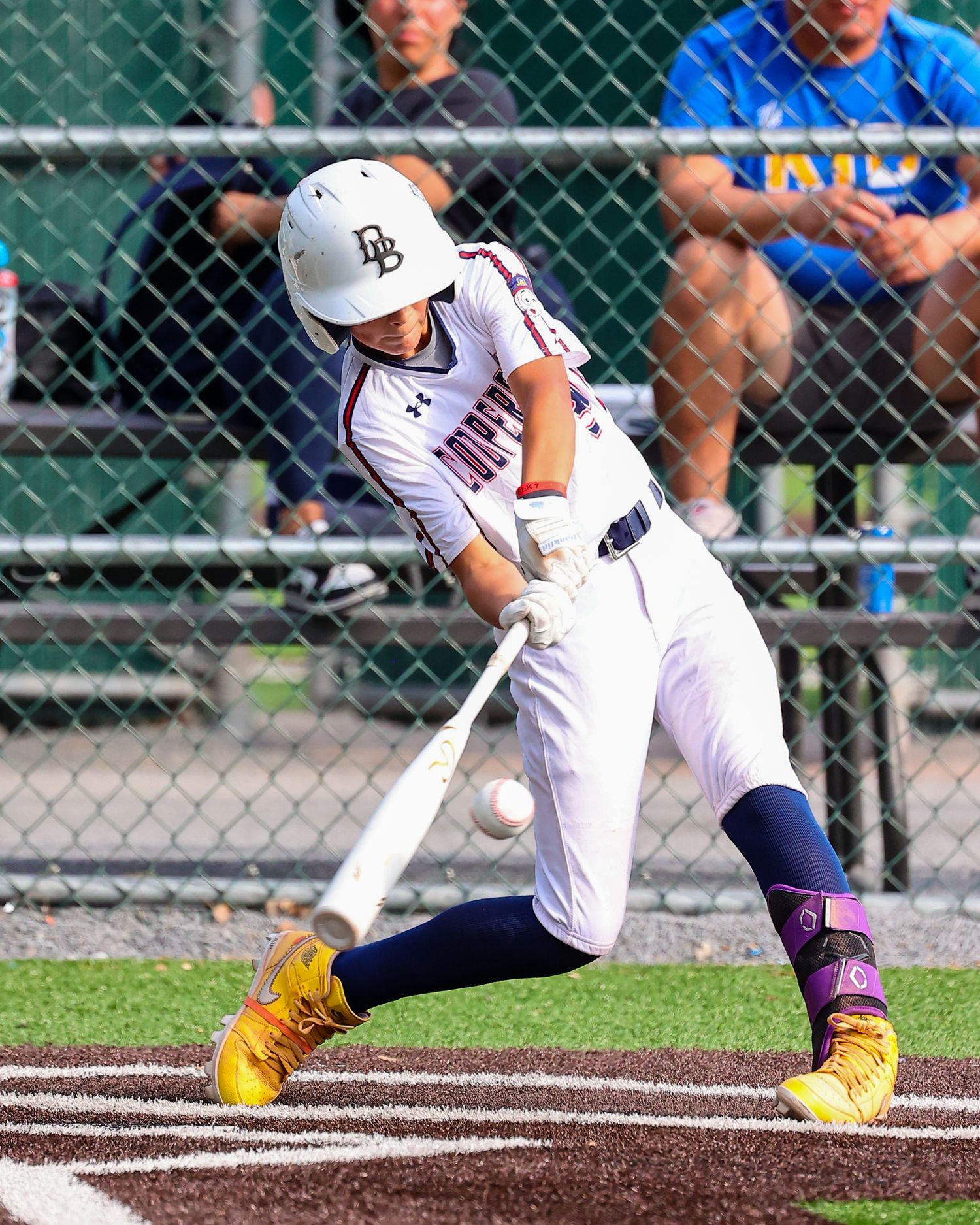 Youth baseball player in white uniform makes contact with ball during batting practice.