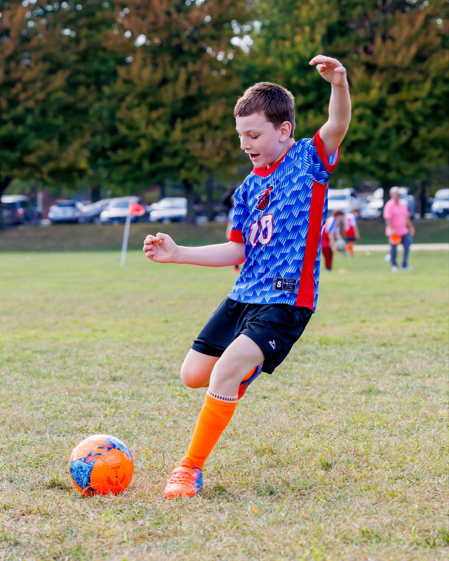 Young boy in blue soccer uniform kicking orange ball on green grass field during youth soccer game.