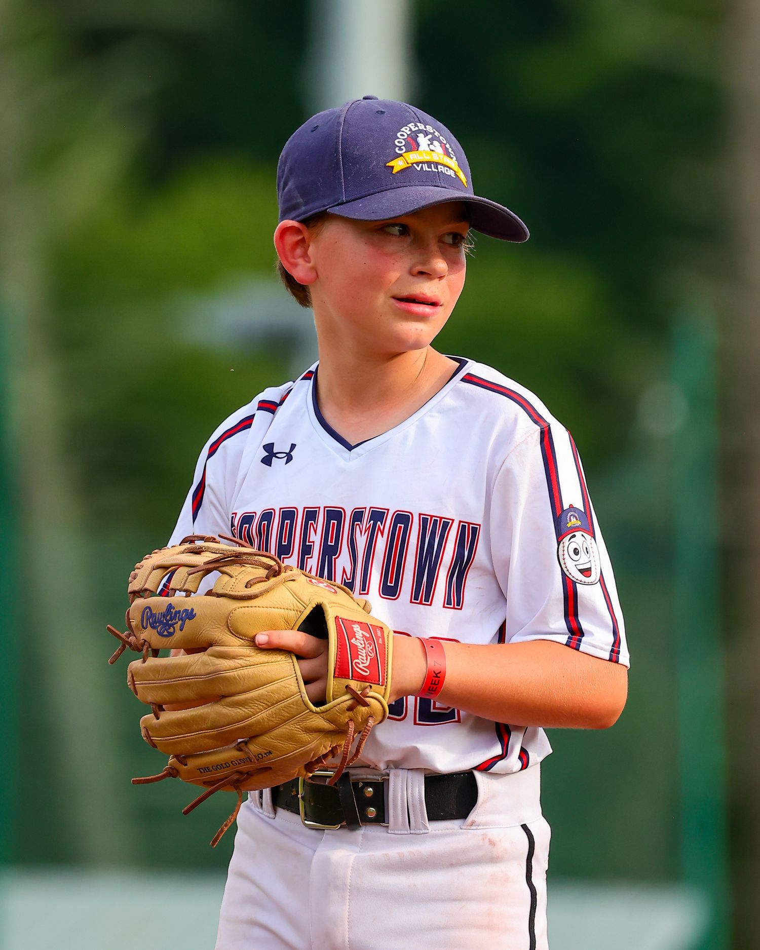 Young baseball player in white uniform and blue cap stands ready in fielding position during a game.