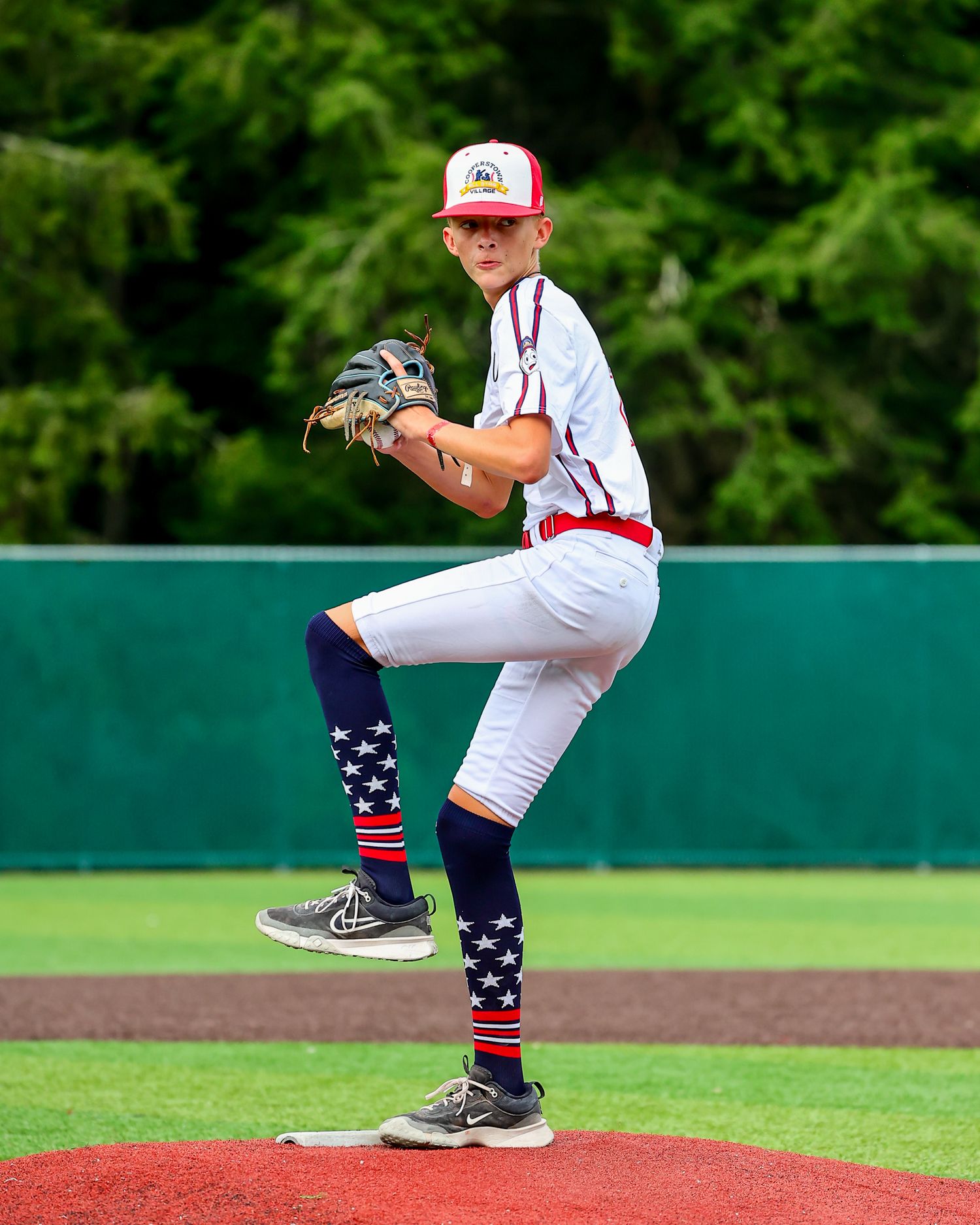 Baseball pitcher on mound in white uniform with red cap winds up for pitch on green field.