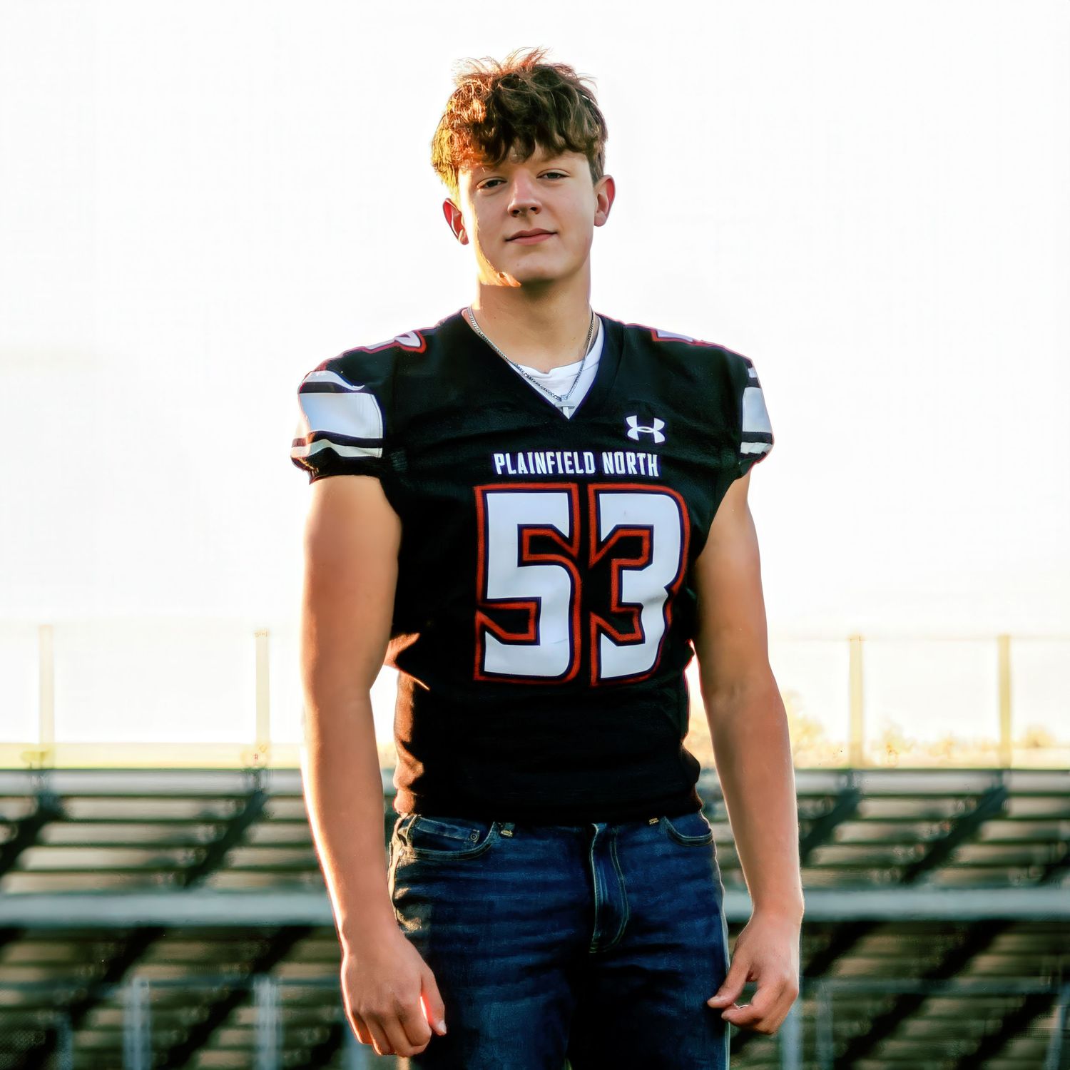 High school football player in black jersey poses on field.