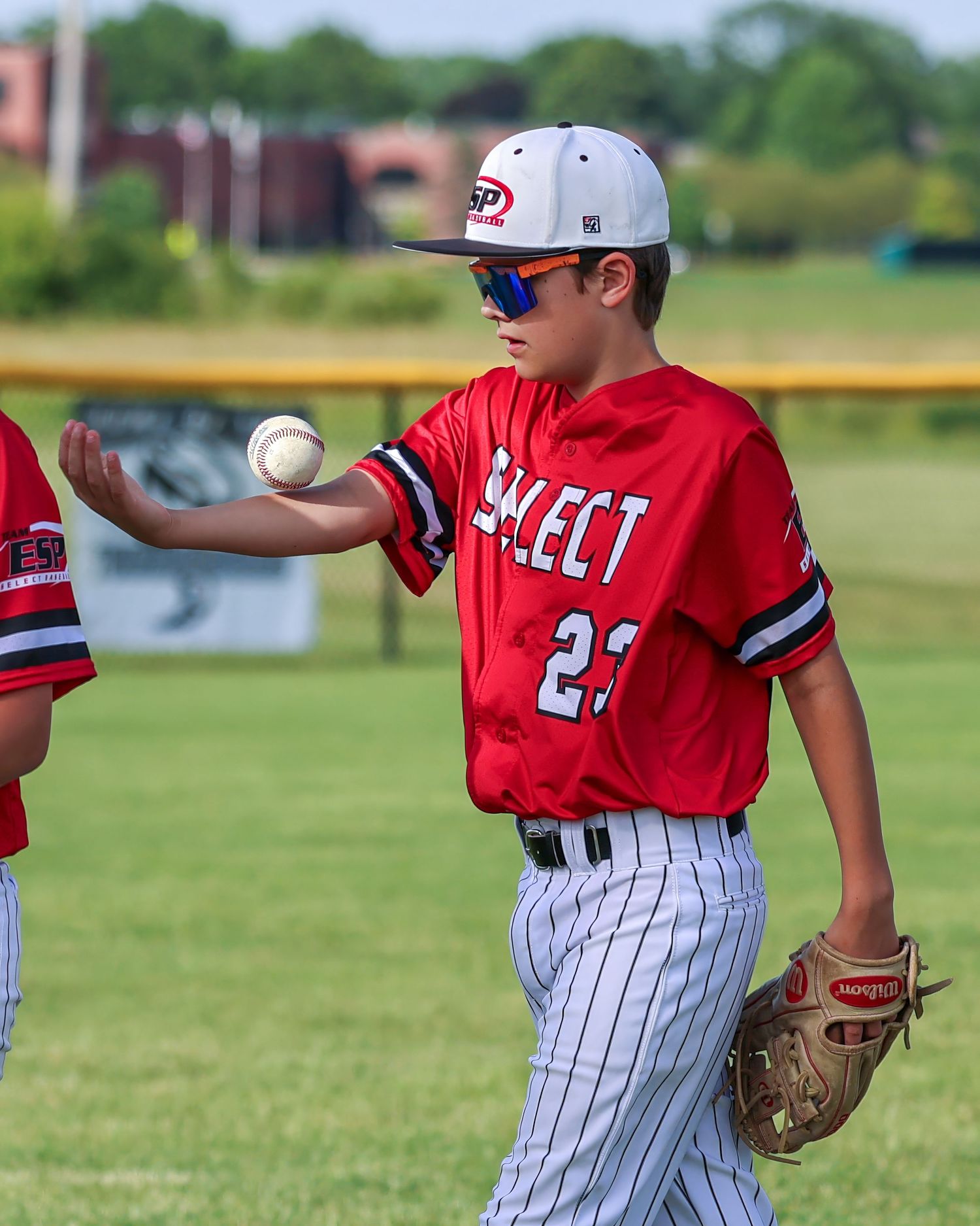 Baseball player in red uniform tosses baseball while wearing mitt on field.