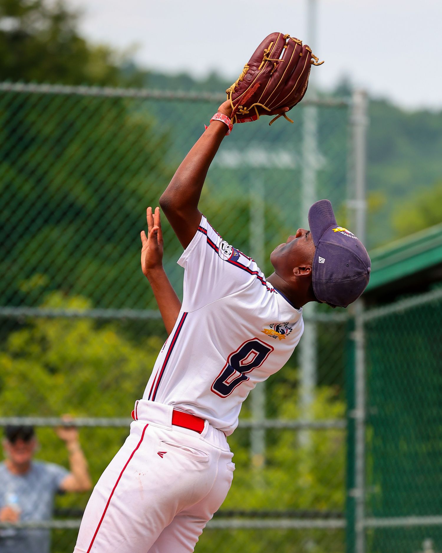 Baseball player wearing white uniform and navy cap makes a leaping catch with brown leather glove during game.