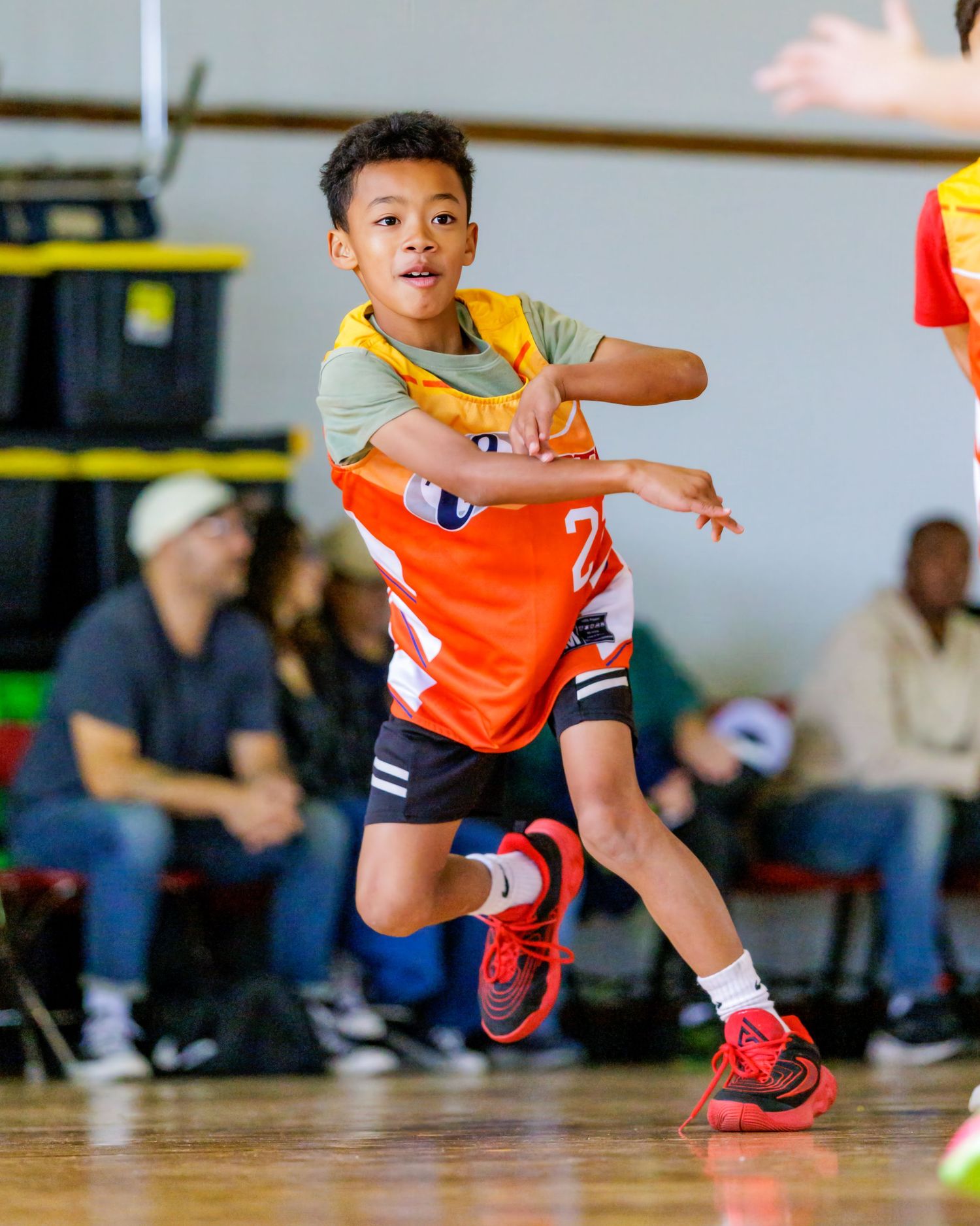 Young athletes in orange jerseys practice dodging and jumping drills in a gymnasium.