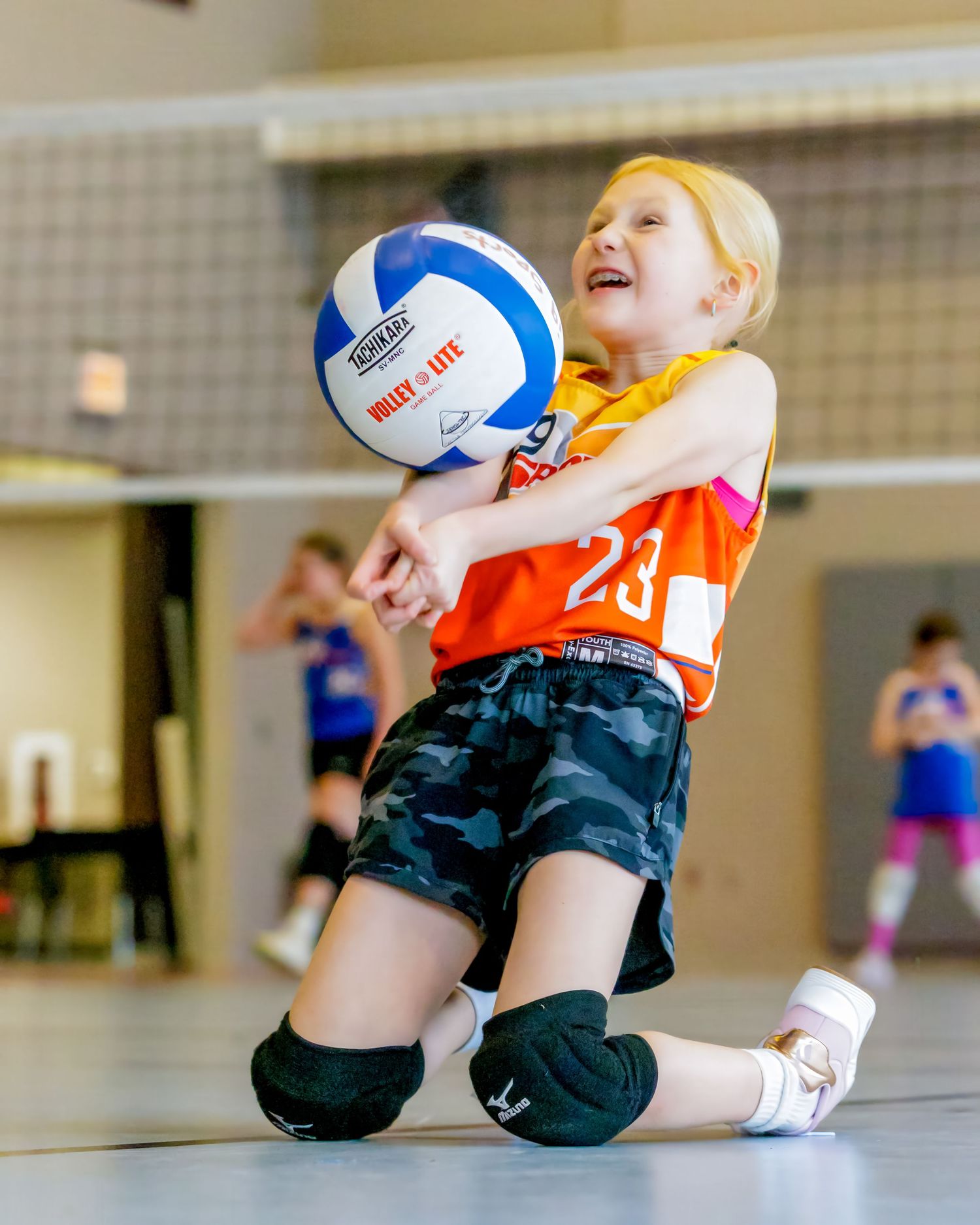 A volleyball player dives low to save the ball during an intense indoor match.