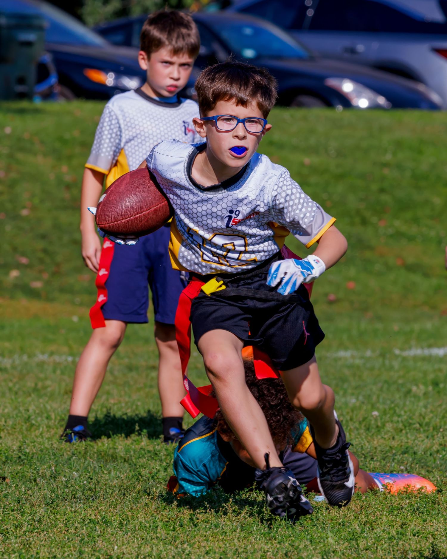 Youth flag football players line up in ready positions on a sunny grass field during a game.