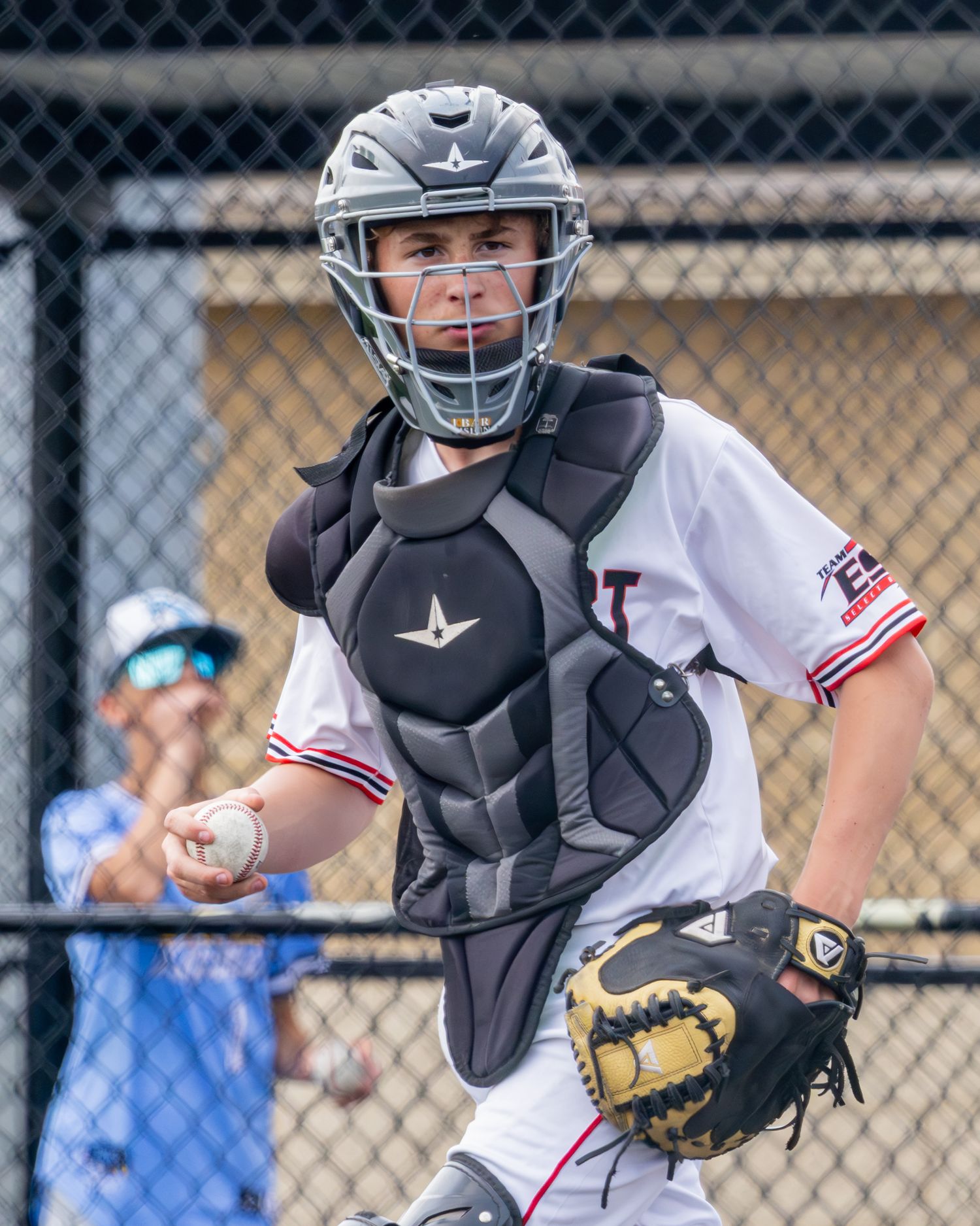 Baseball catcher in protective gear crouches behind home plate in ready position during game.