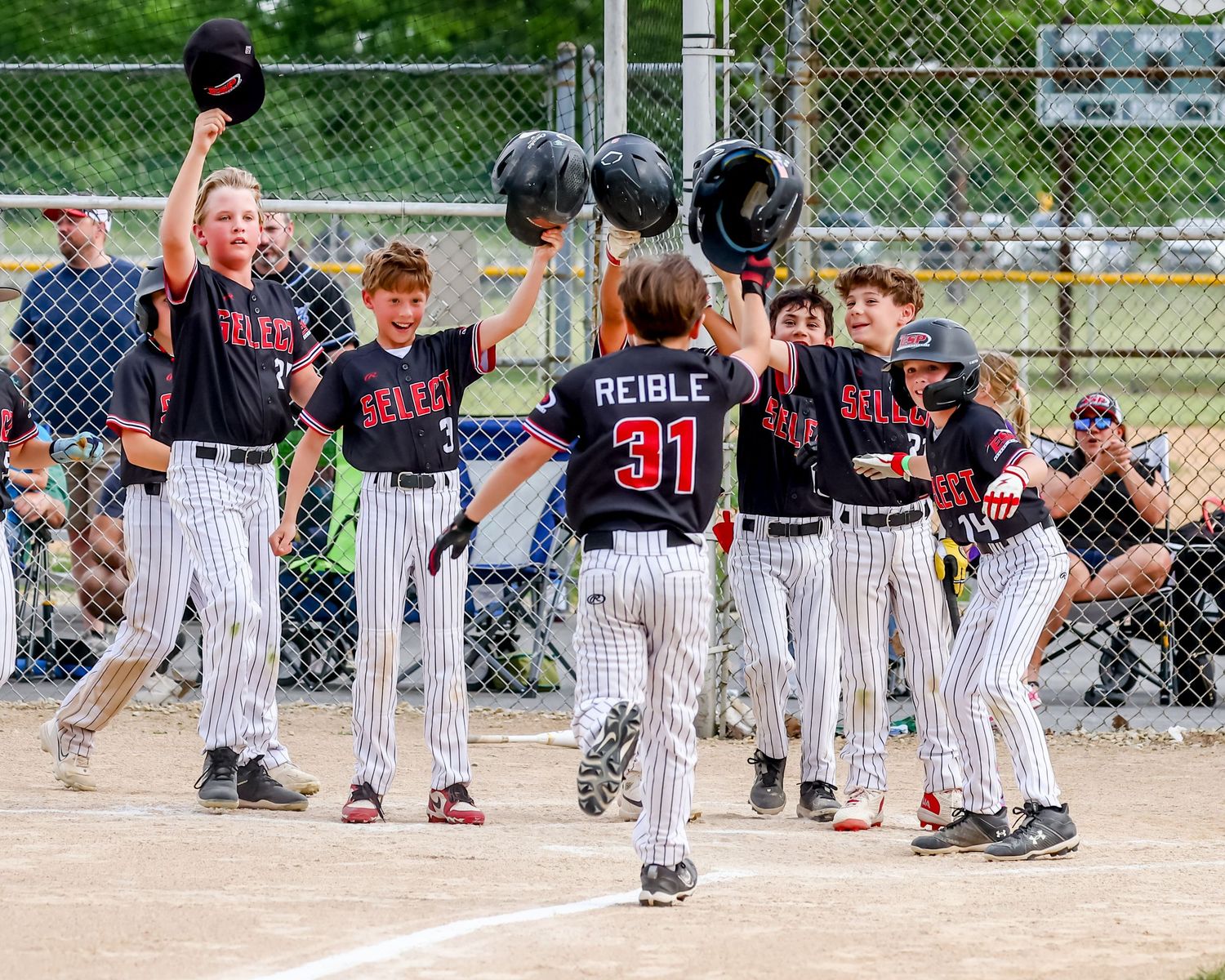 Baseball players in striped uniforms wait in dugout during a youth league game on a sunny day.