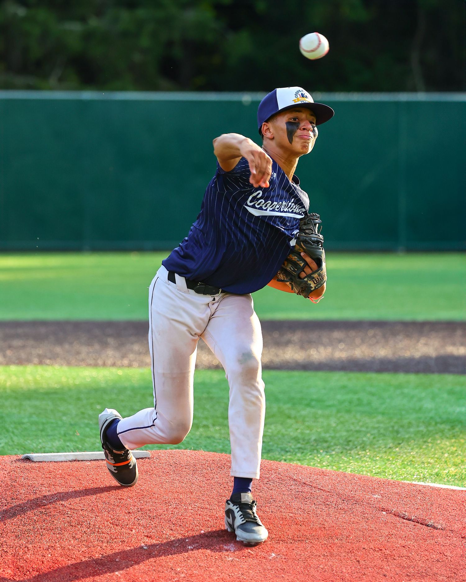 Baseball pitcher in navy uniform demonstrates throwing motion sequence on red turf field during training session.