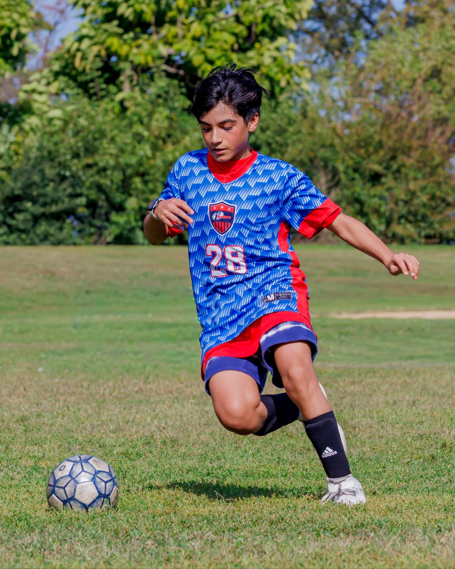 Soccer player in blue patterned jersey practicing footwork with a ball on grass field.