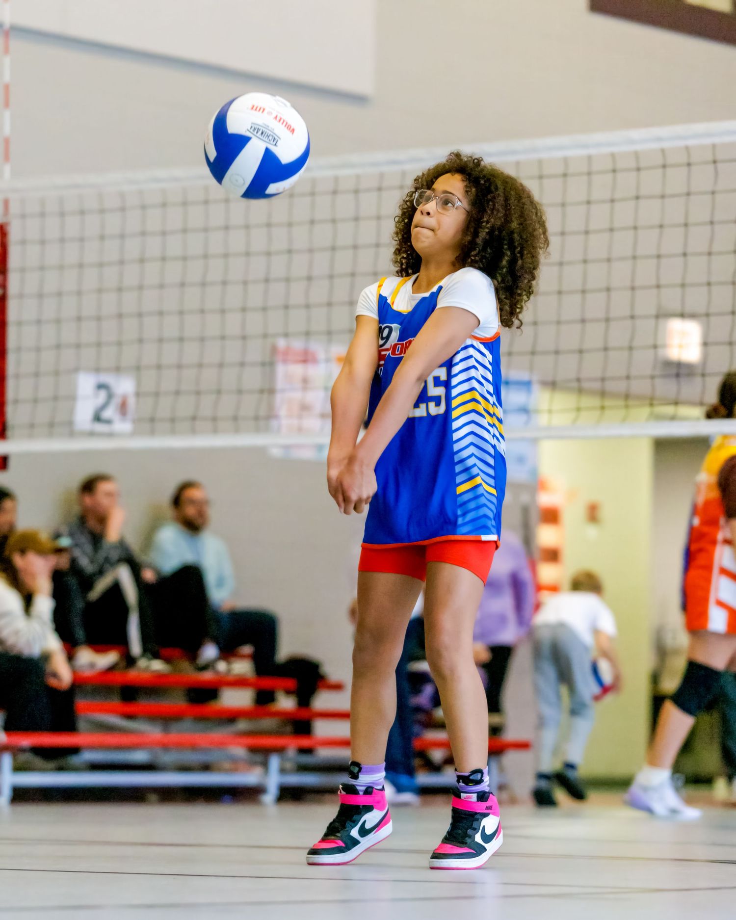 Volleyball players in blue and white uniforms jumping and positioning near the net during an indoor match.