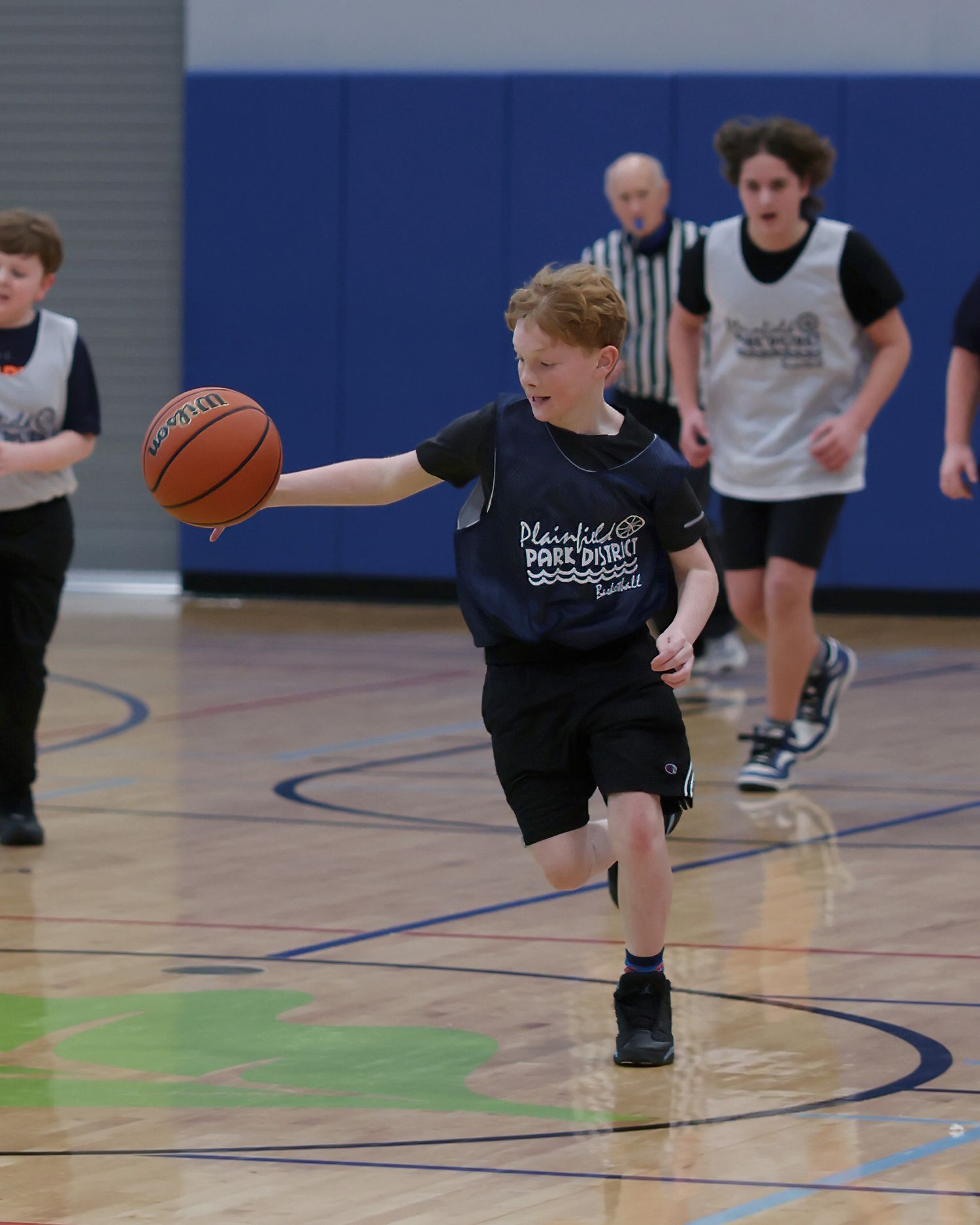 Young basketball players practice dribbling drills in a blue-floored gymnasium during training.