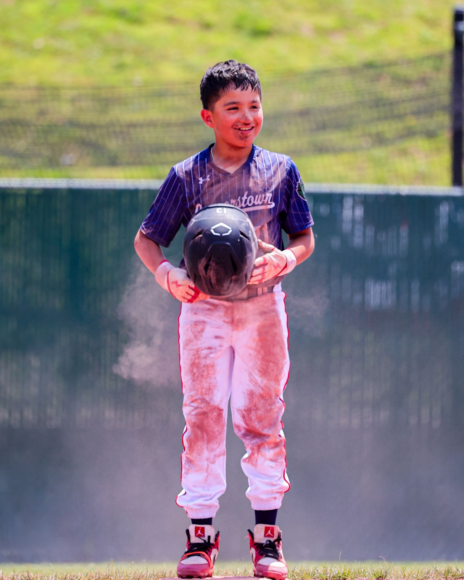 A child in white pants plays on a misty sports field during a sunny day.