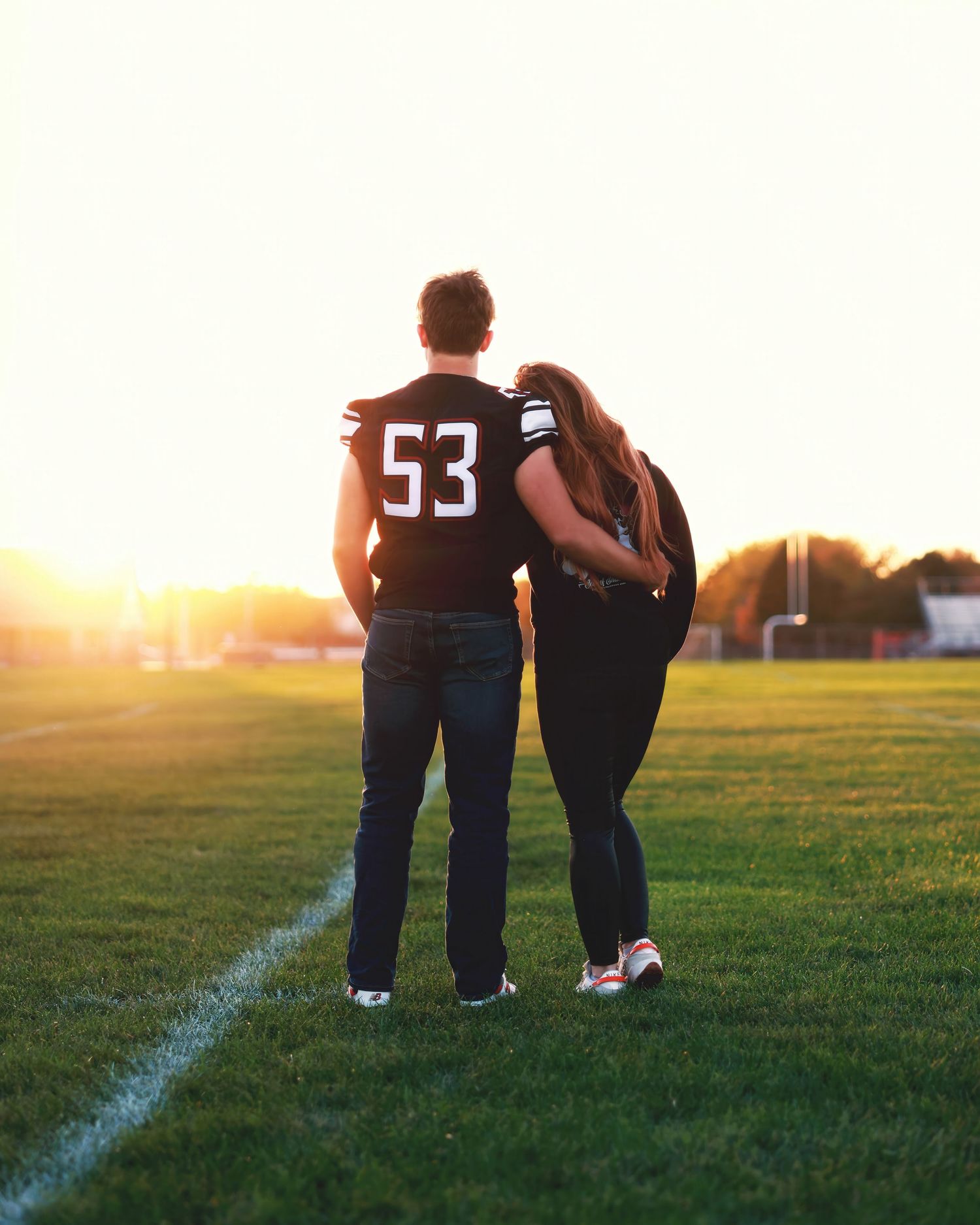 Two people stand close together on a grassy field at sunset with white lines marked on the ground.