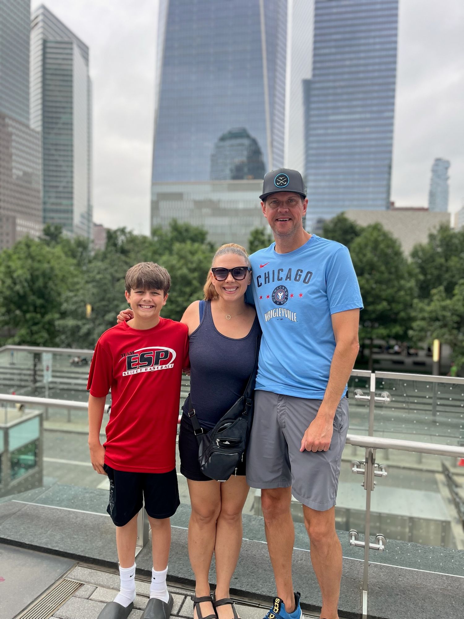 A family group stands together at a scenic overlook with modern city buildings visible in the background.