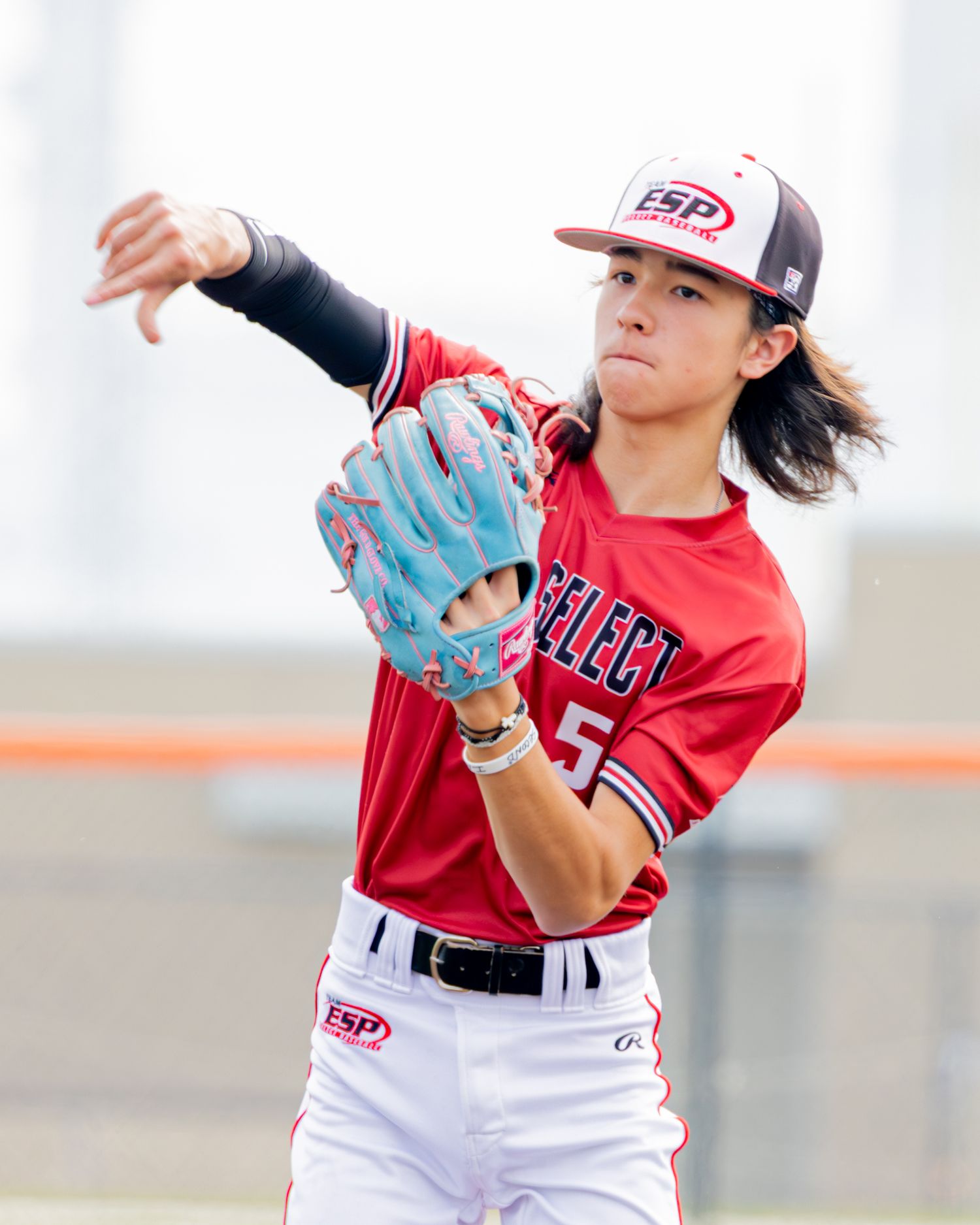 Youth softball player wearing red and white uniform winds up for a pitch on outdoor field during game.