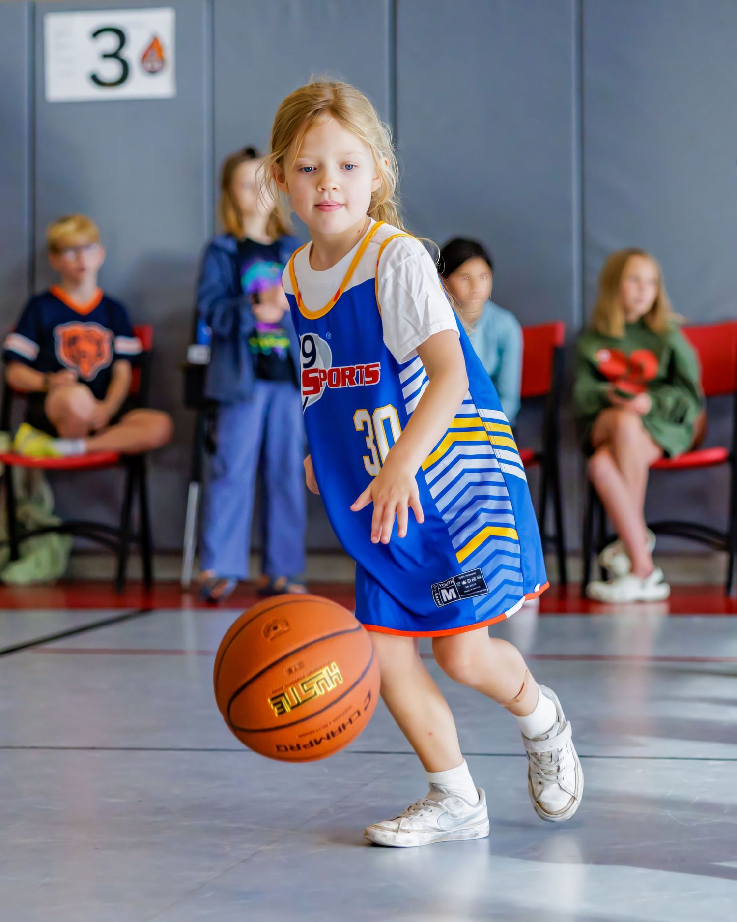 Young basketball players dribbling orange basketballs during practice in a gymnasium with blue uniforms.