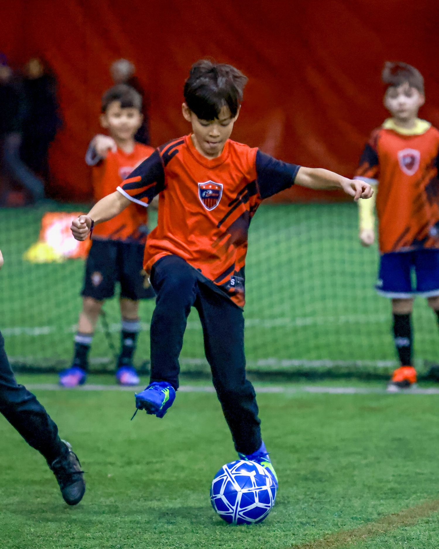 Soccer practice sequence shows young player in orange jersey kicking a blue ball on grass field during training.