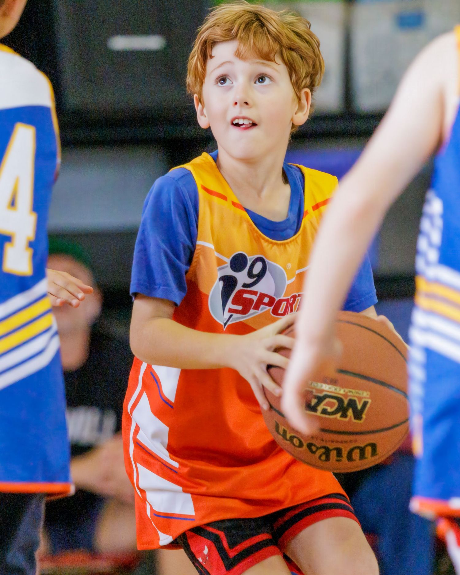 Youth basketball players in orange and blue uniforms compete for the ball during a game.
