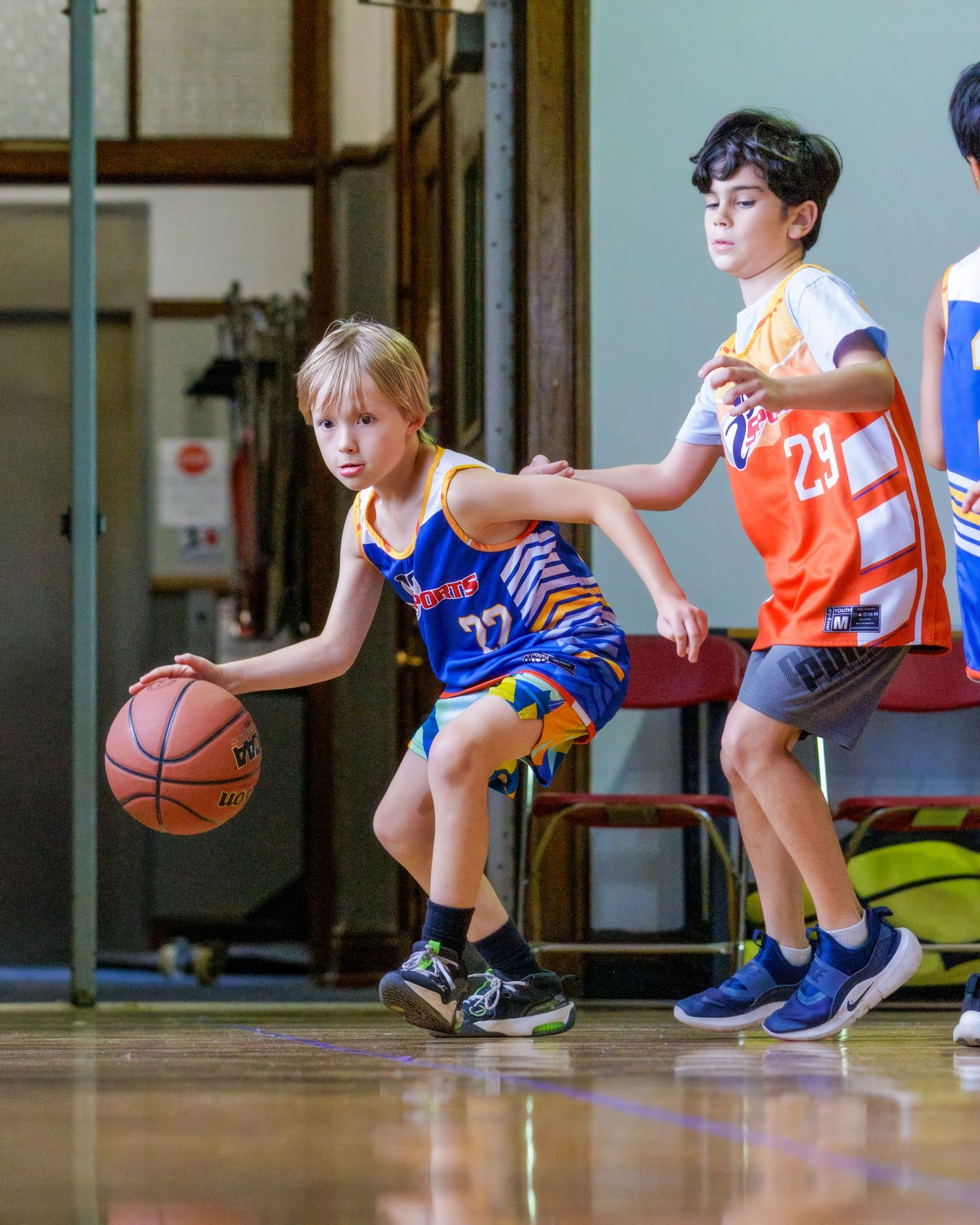 Young basketball players in blue and orange uniforms practice dribbling drills on a wooden court during training.