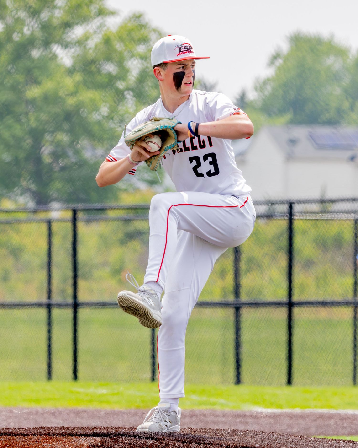 Baseball pitcher in white uniform winds up for delivery in follow through motion during game on grass field.