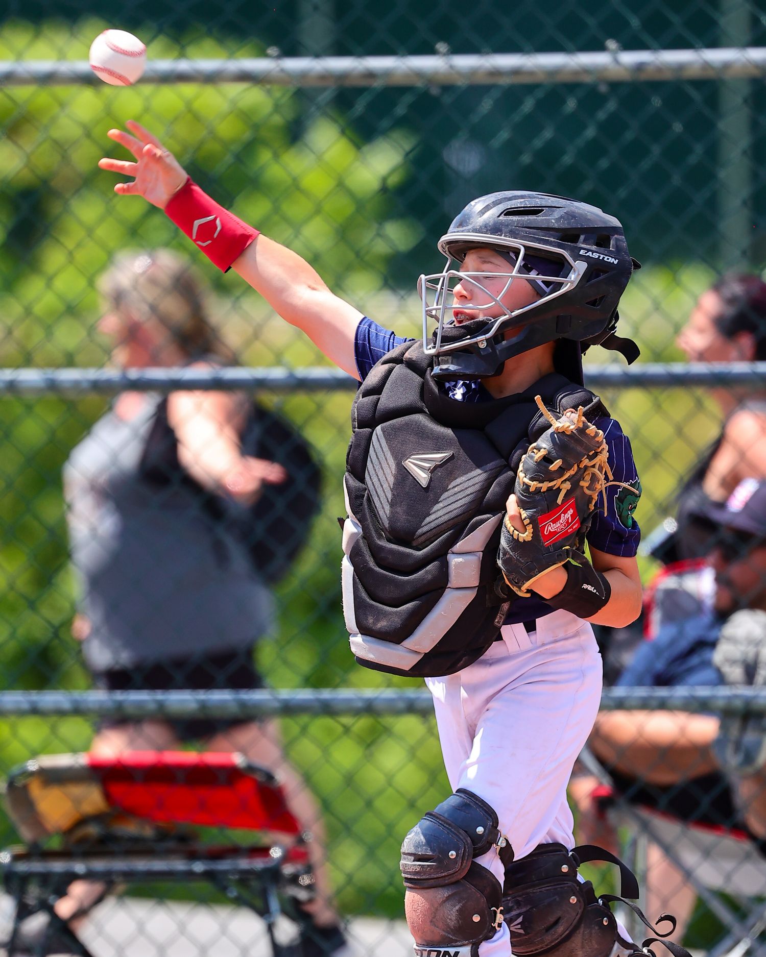 Baseball catcher in protective gear crouches behind home plate during a game on a sunny day.