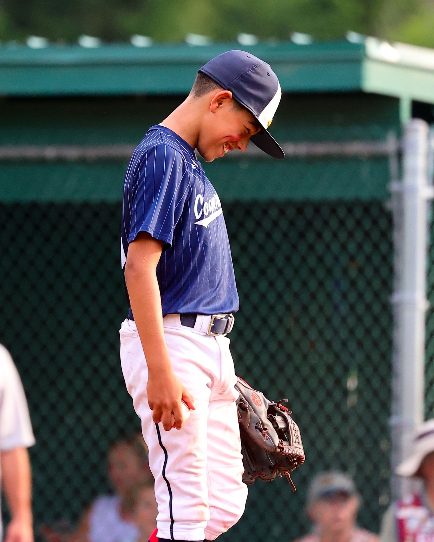 Baseball player in navy uniform and cap looks down at the field during a game.