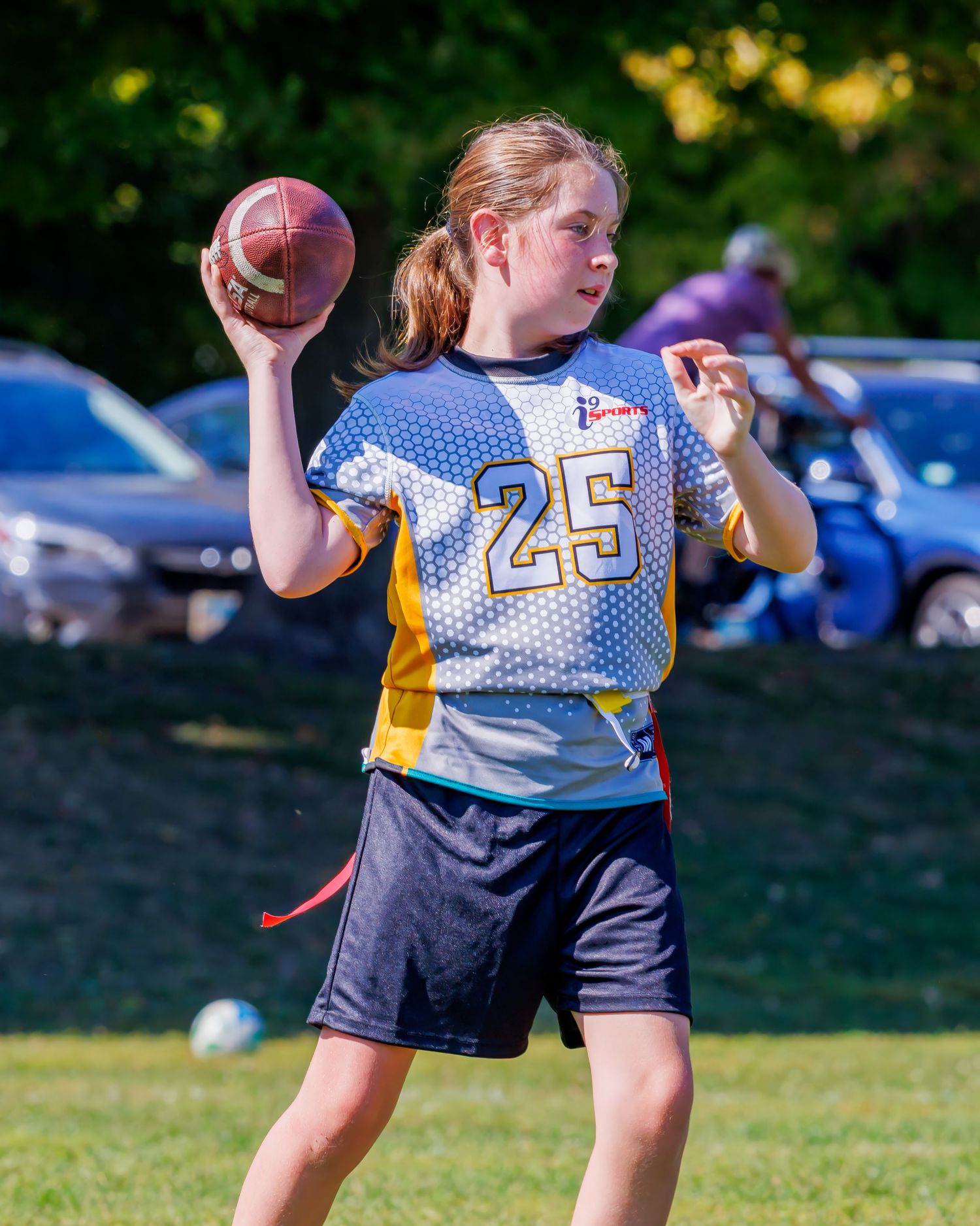 Flag football player in yellow and white jersey throws a pass during an outdoor game on a sunny day.