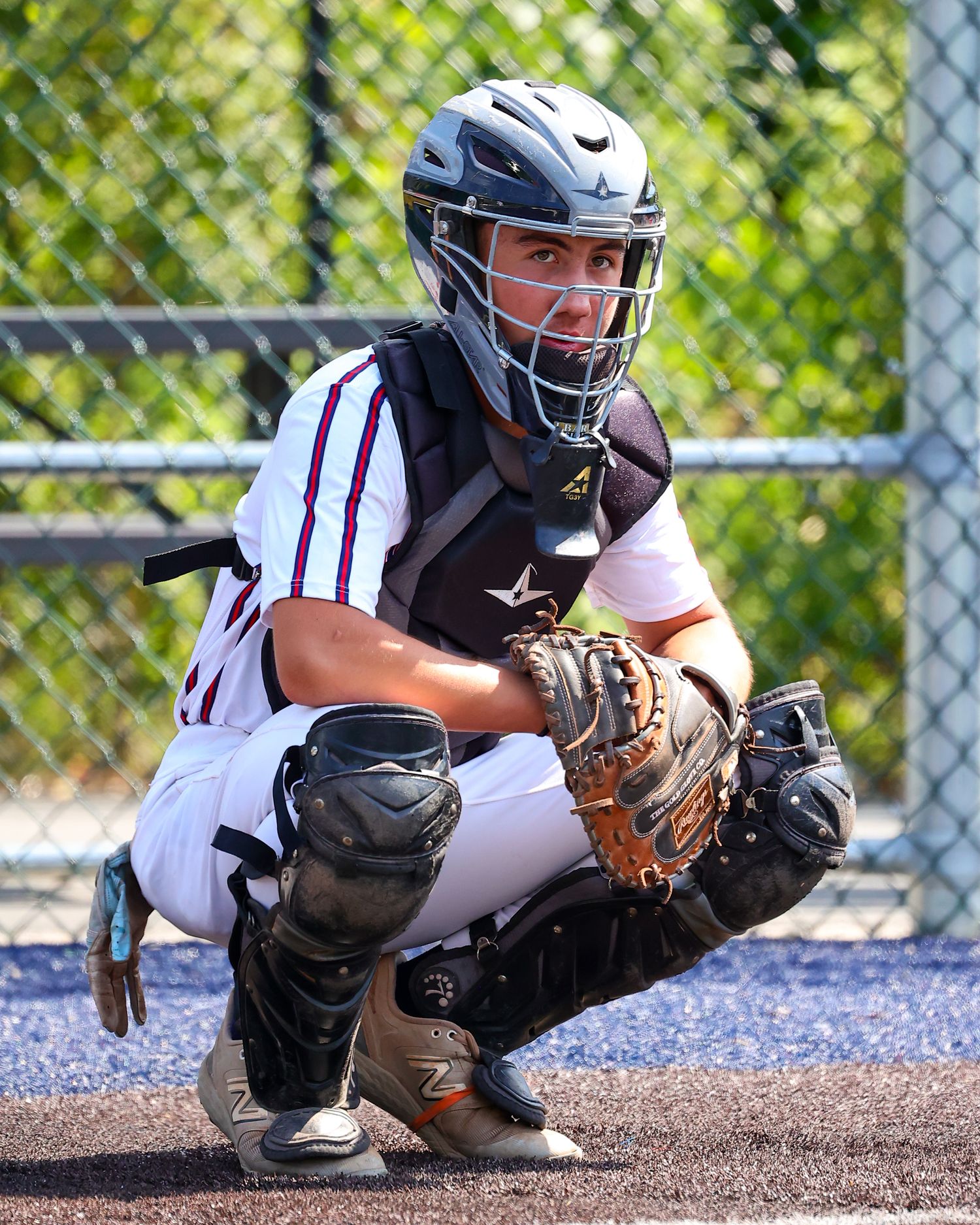 Baseball catcher in protective gear crouches behind home plate during a game.