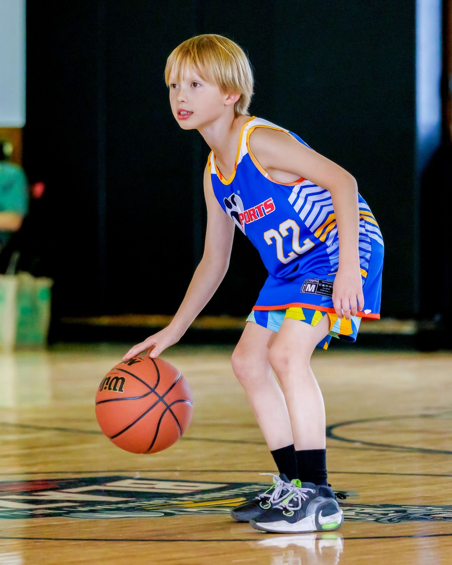 Young boy in blue number 22 basketball jersey dribbling a ball on an indoor court.