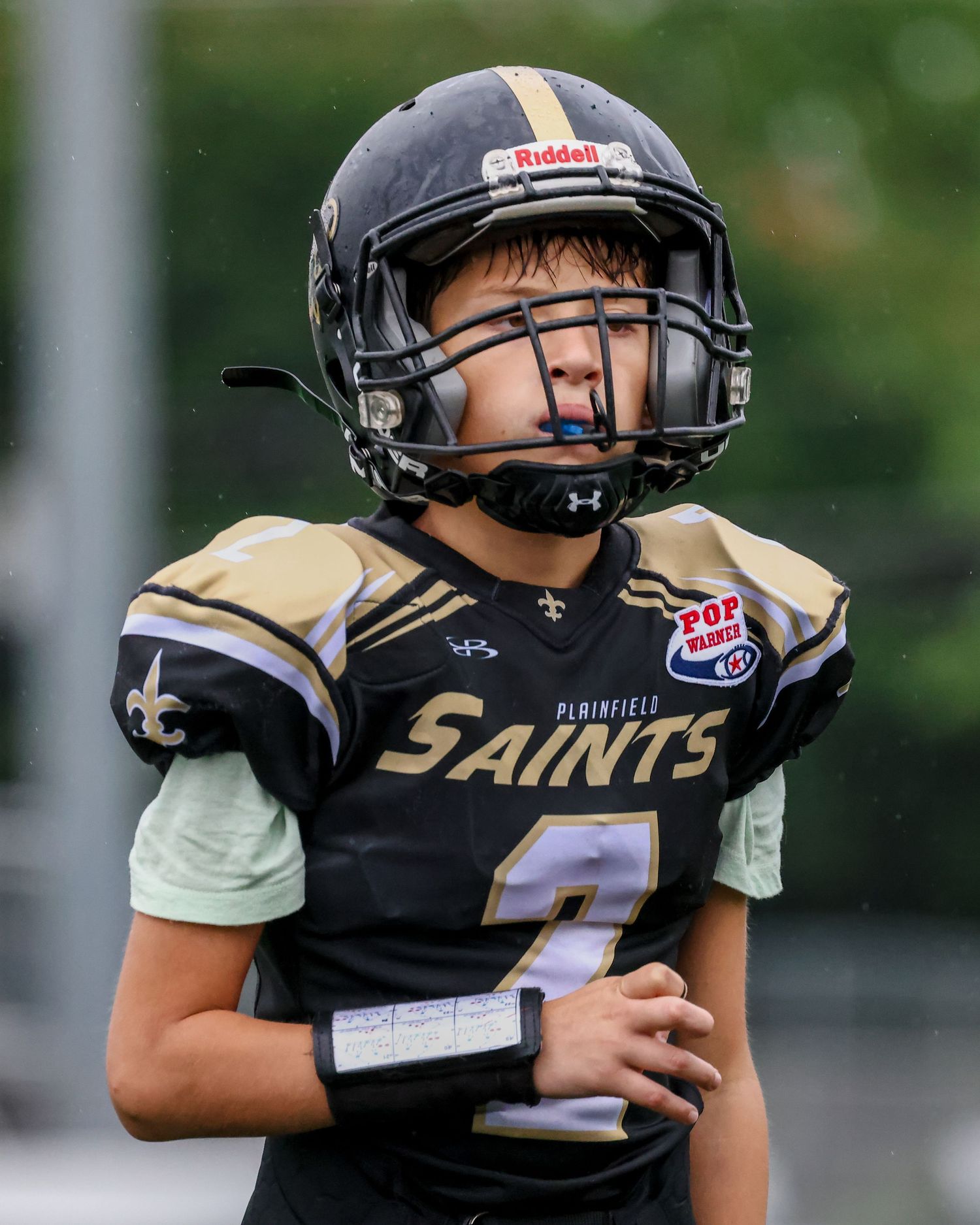 Youth football player wearing black Saints uniform and helmet during game.