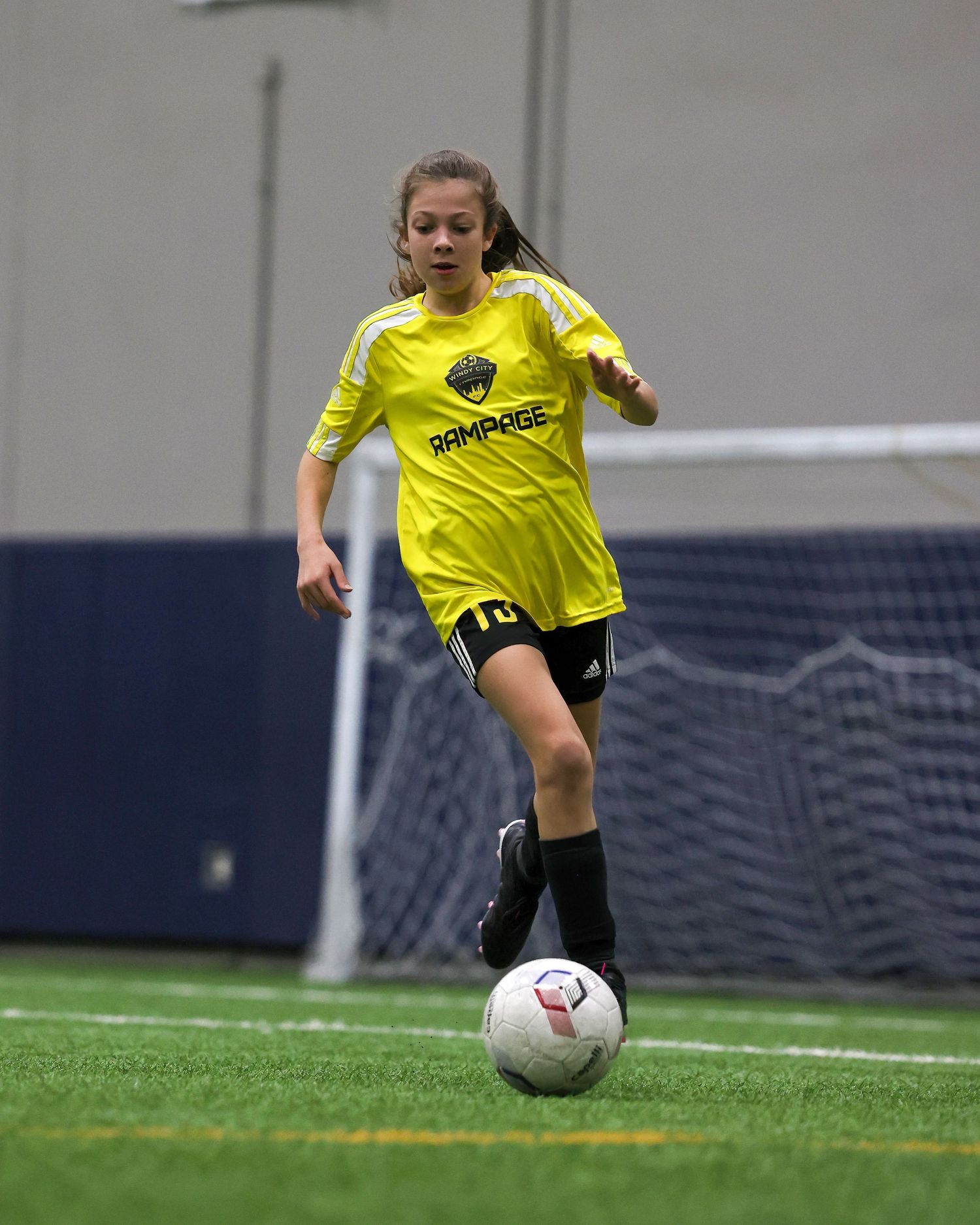 Soccer player in yellow jersey dribbles ball on indoor turf field during practice session.