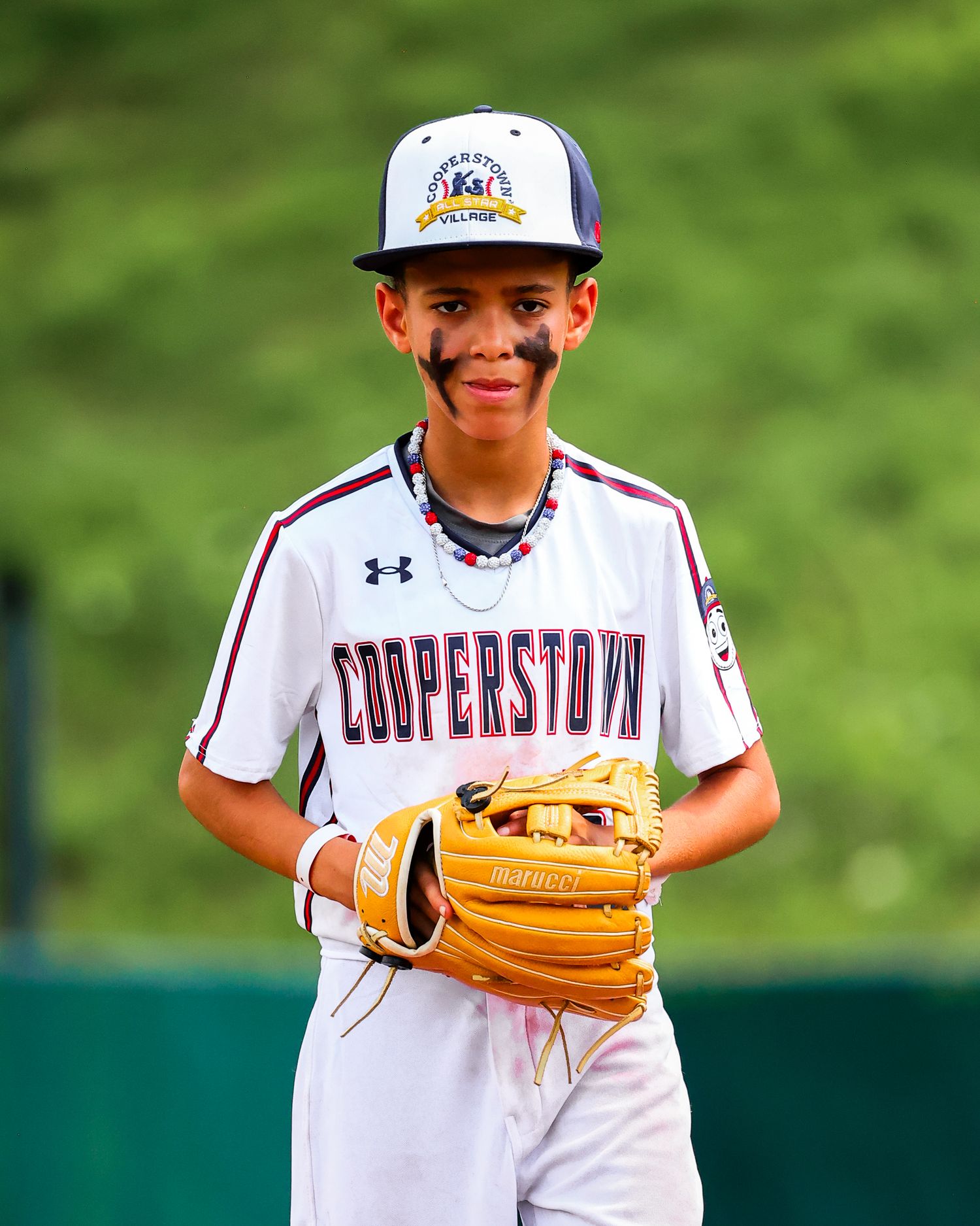 Young baseball player in white uniform and orange cap smiles while holding up a tan leather baseball glove.