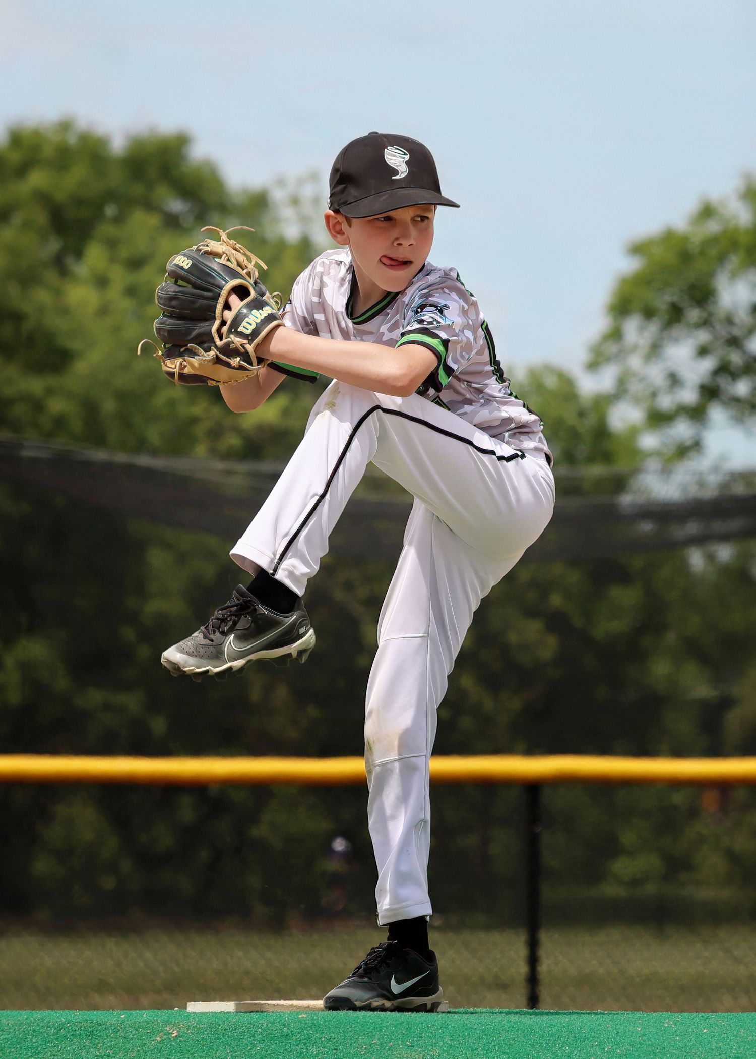 Youth pitcher in white uniform demonstrates pitching windup on mound.