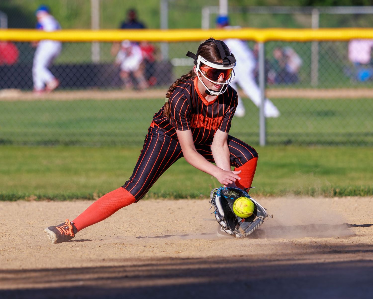 Softball player in black and orange uniform fielding a ground ball during a competitive game.