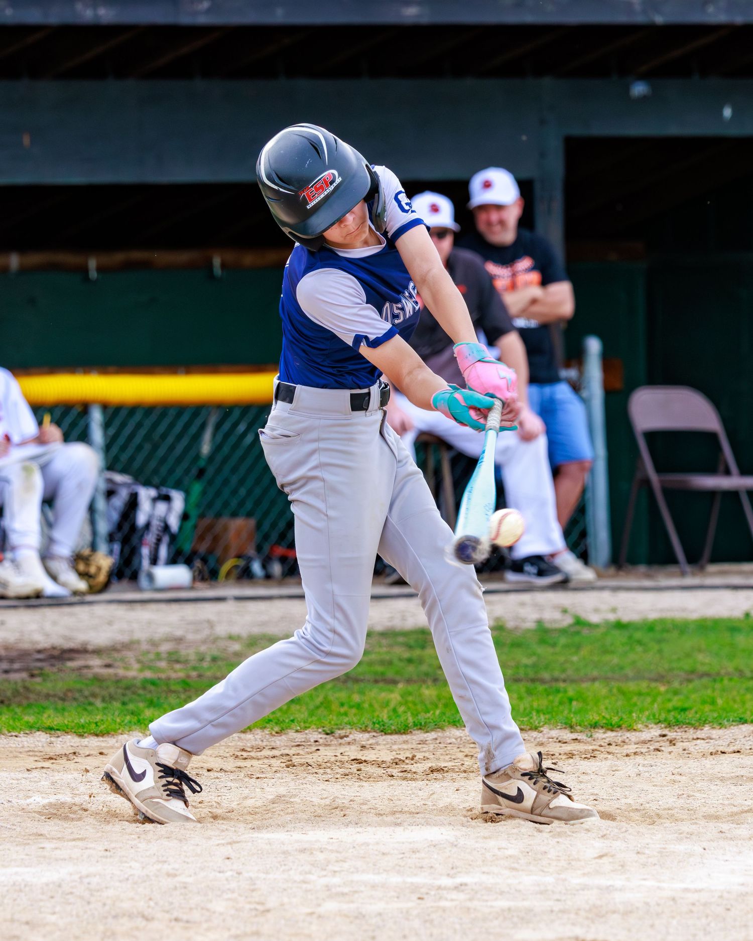 Young baseball player in blue uniform swinging bat during a youth league game on a dirt infield.