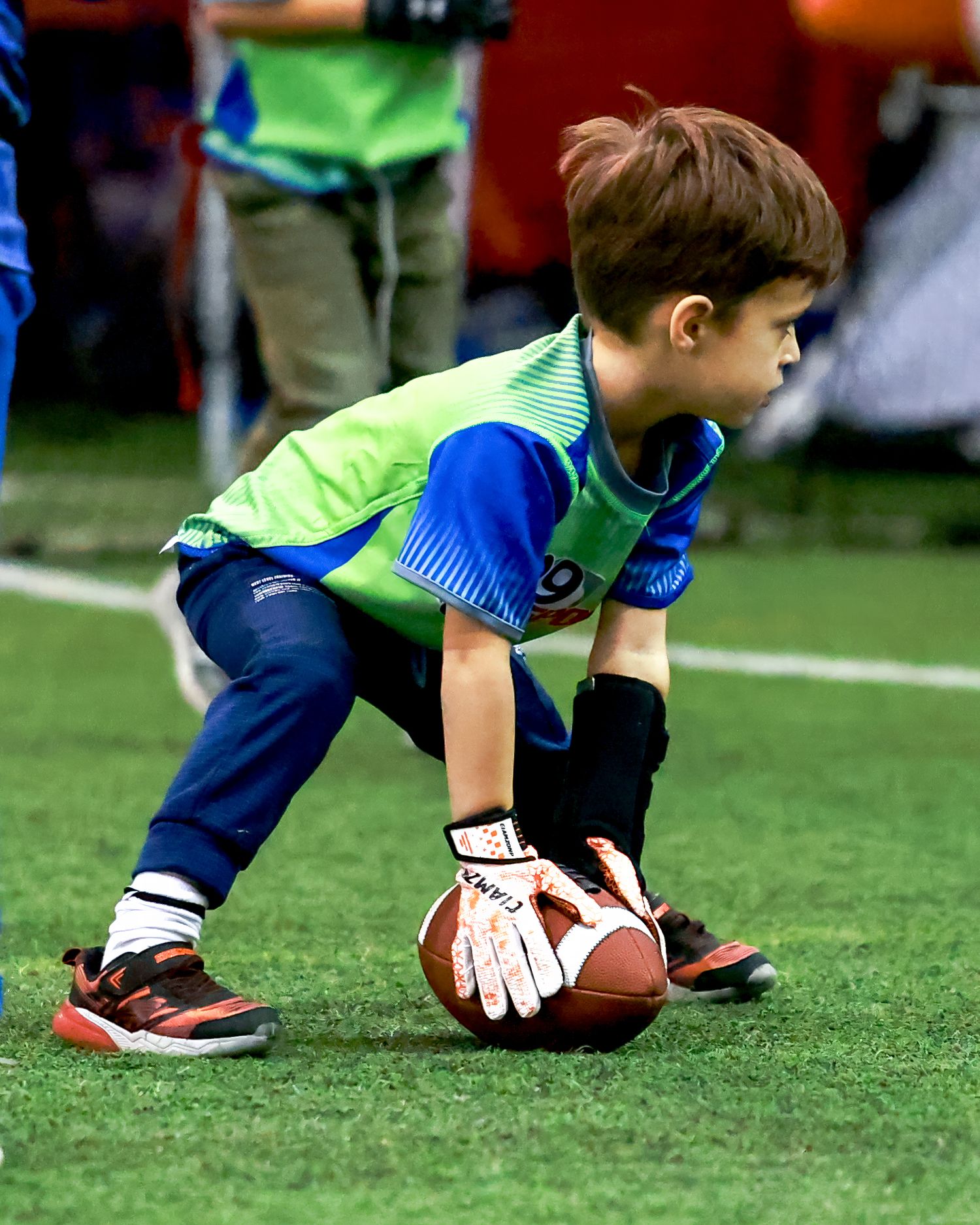 Youth player in green jersey prepares to hike football on indoor playing field.