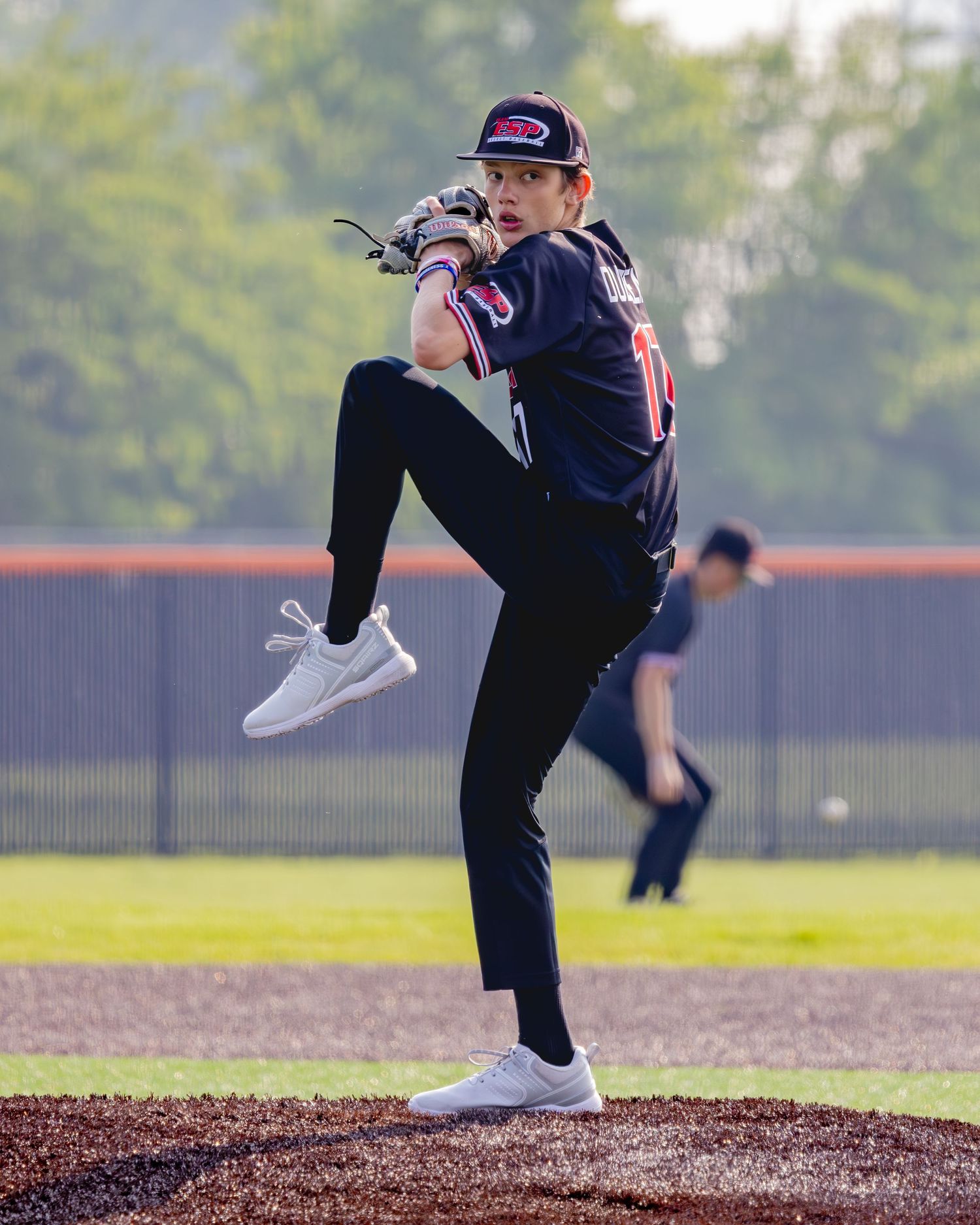 A baseball pitcher demonstrates their windup and follow-through mechanics on the pitcher's mound during practice.