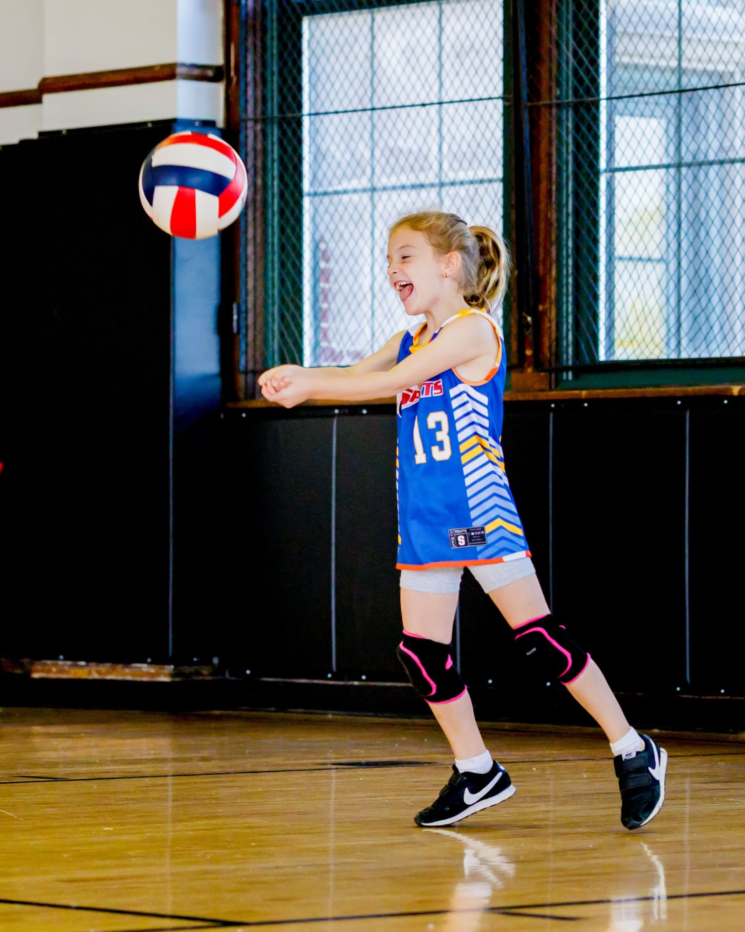 A volleyball player in a blue uniform and headband dives to save the ball during an indoor match.